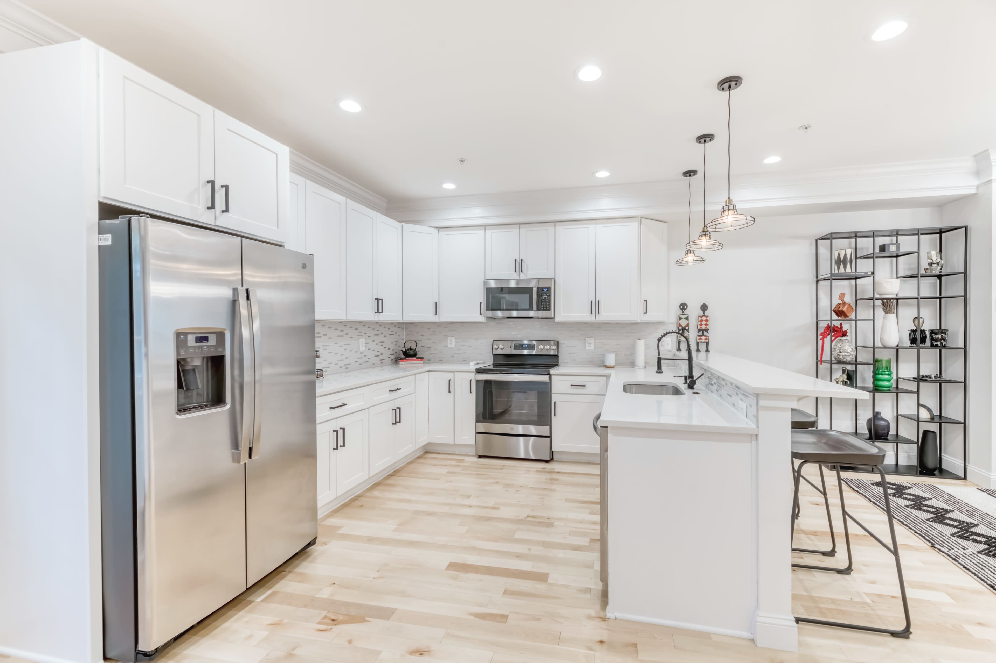 A modern kitchen with stainless steel appliances, white cabinetry, and a bar with two stools.