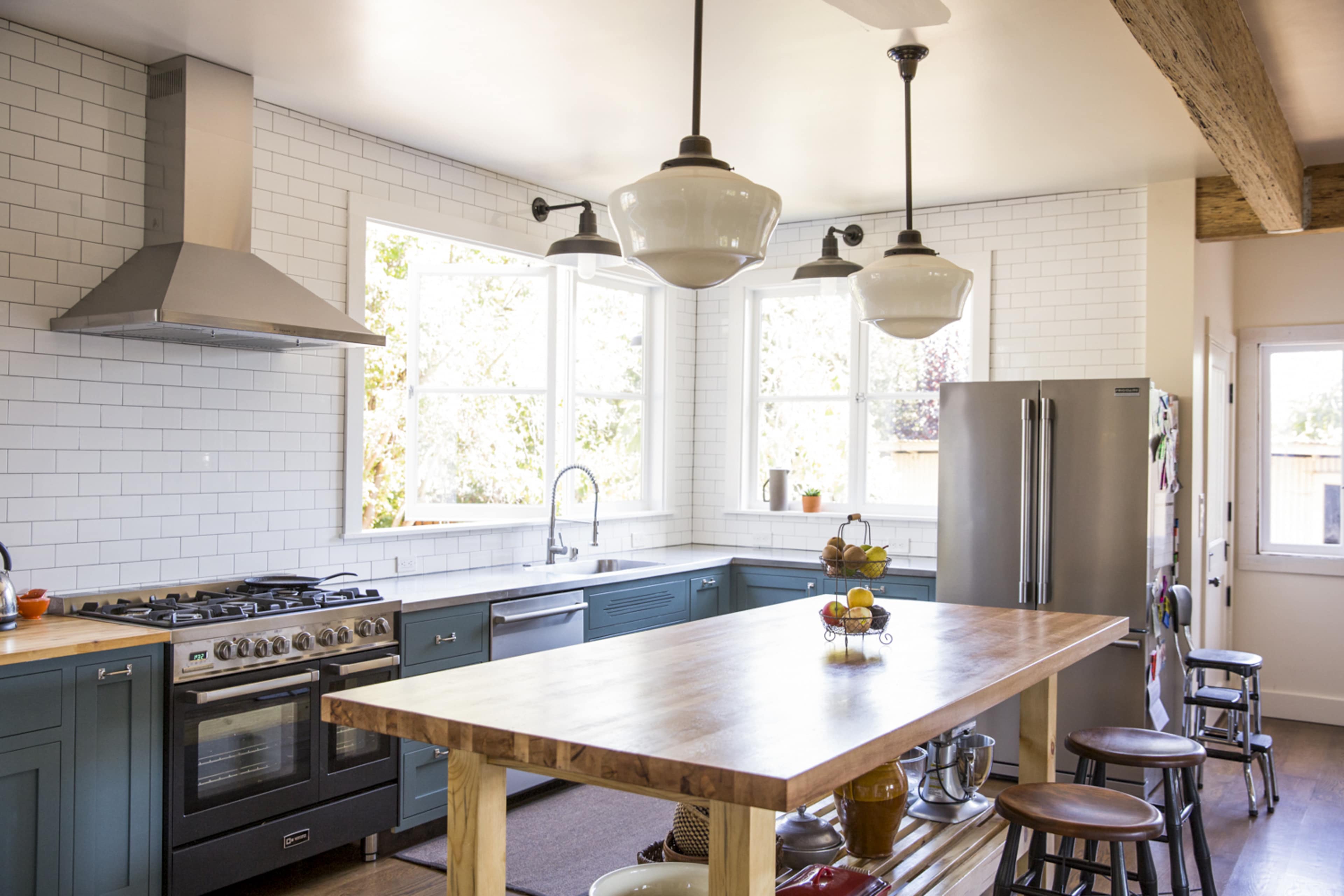A modern kitchen features a large wooden island, stainless steel appliances, and white subway tile walls.