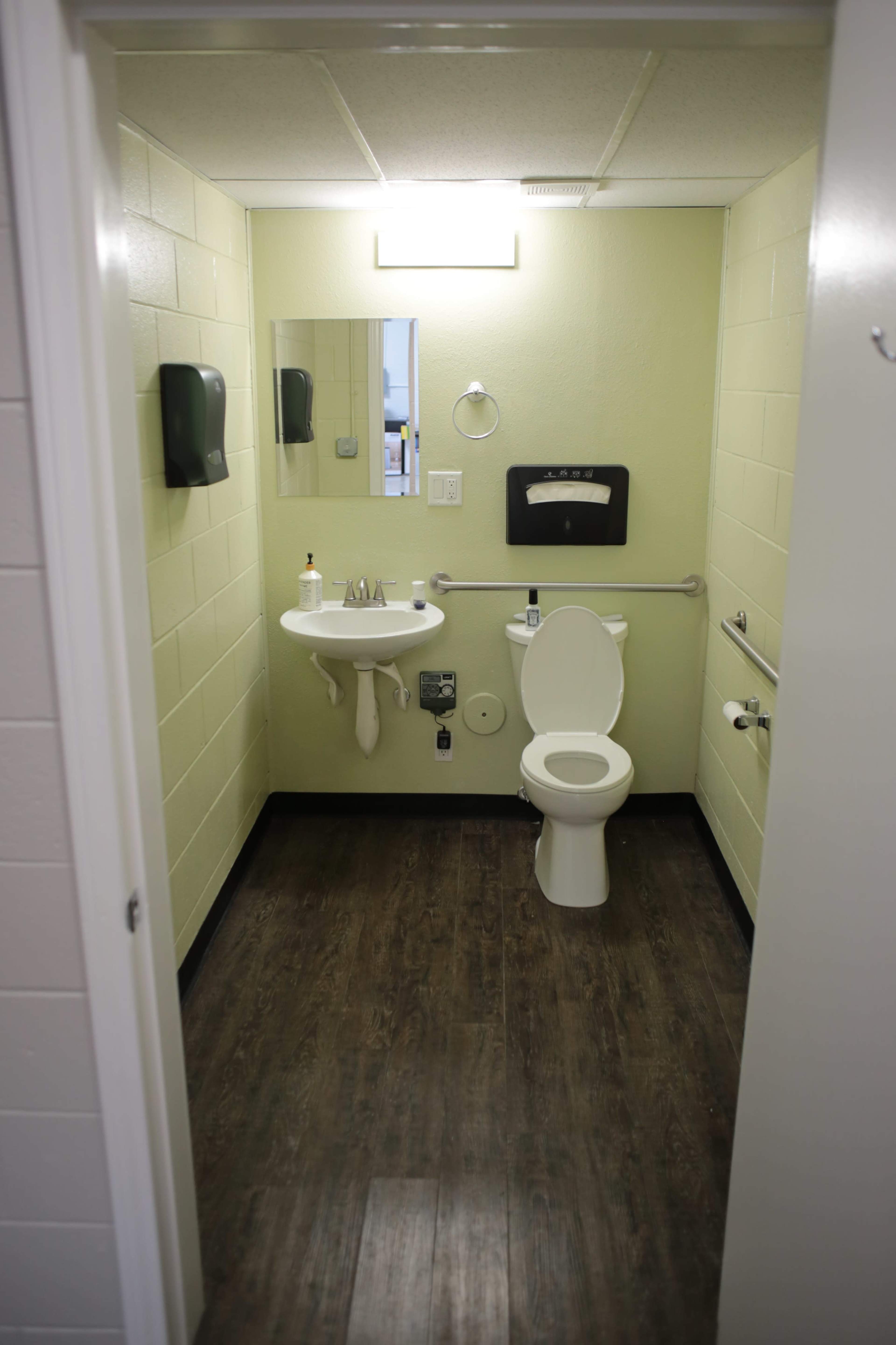 A small restroom with a toilet, sink, and a mirror on the green walls, along with hand dryers and grab bars.