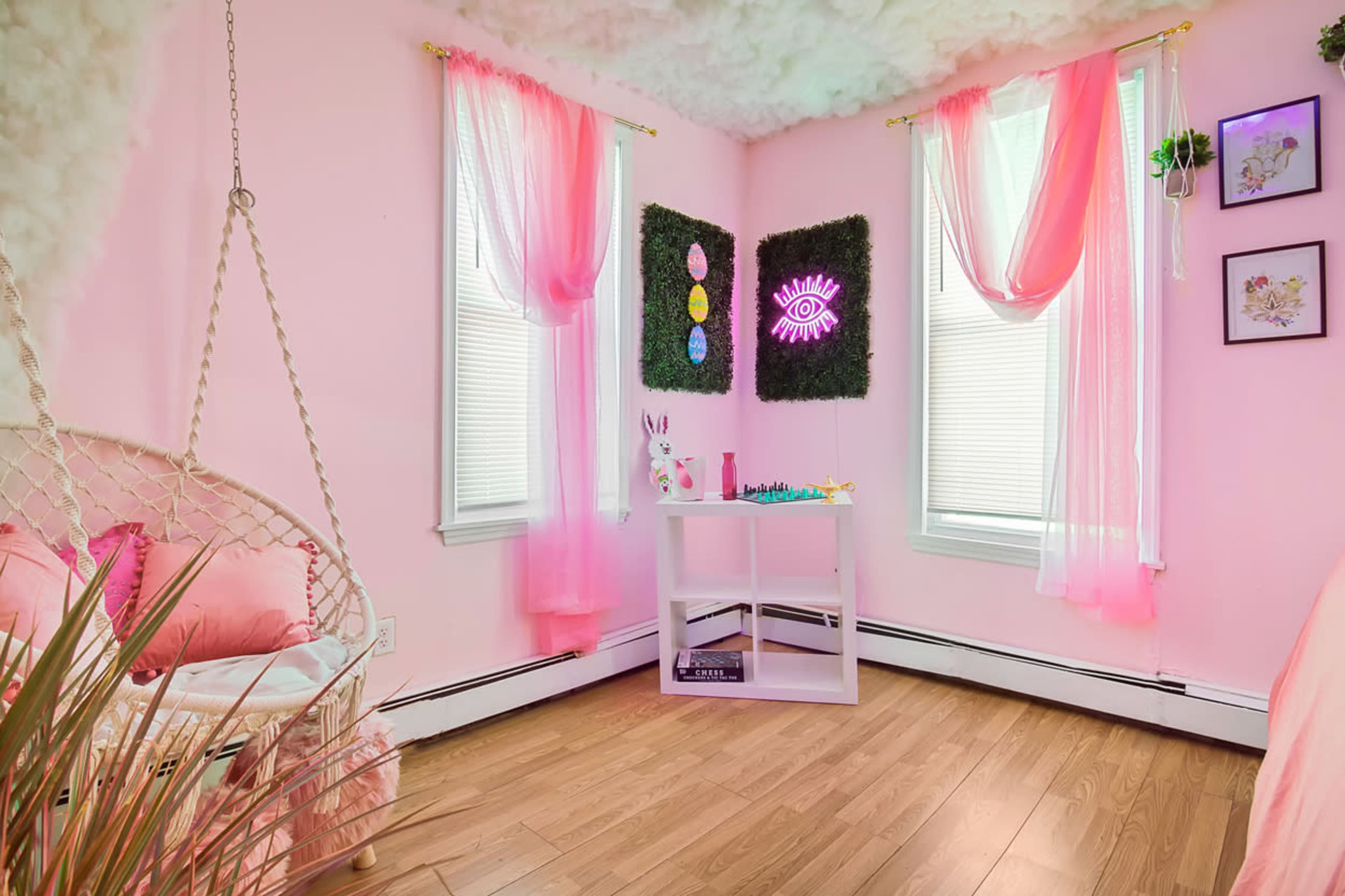 A brightly colored pink room with a hanging chair, decorative plants, and a small white table displaying toys and art.