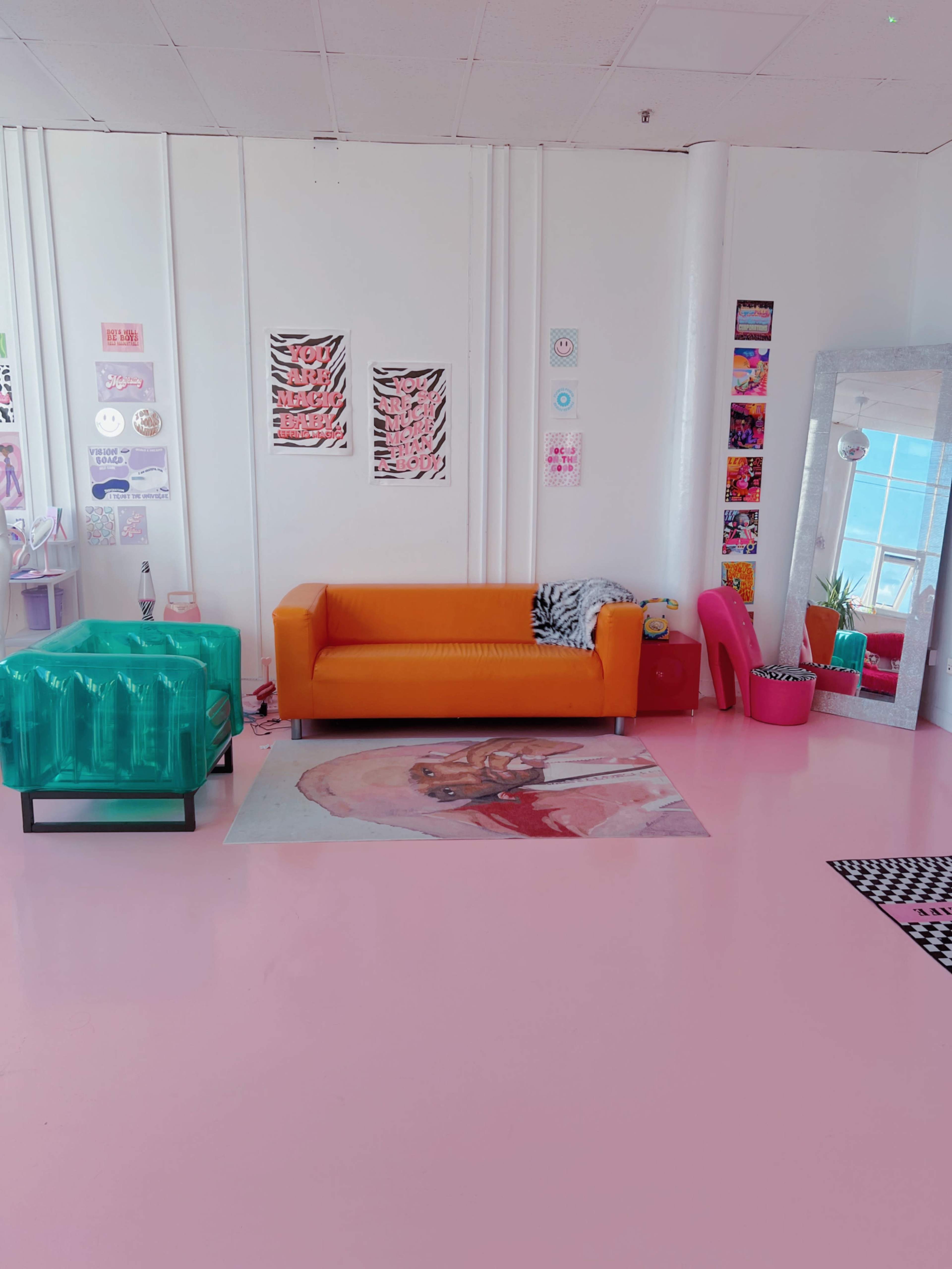 A colorful interior living space featuring an orange sofa, a glass coffee table, a large mirror, and various decorative wall art.