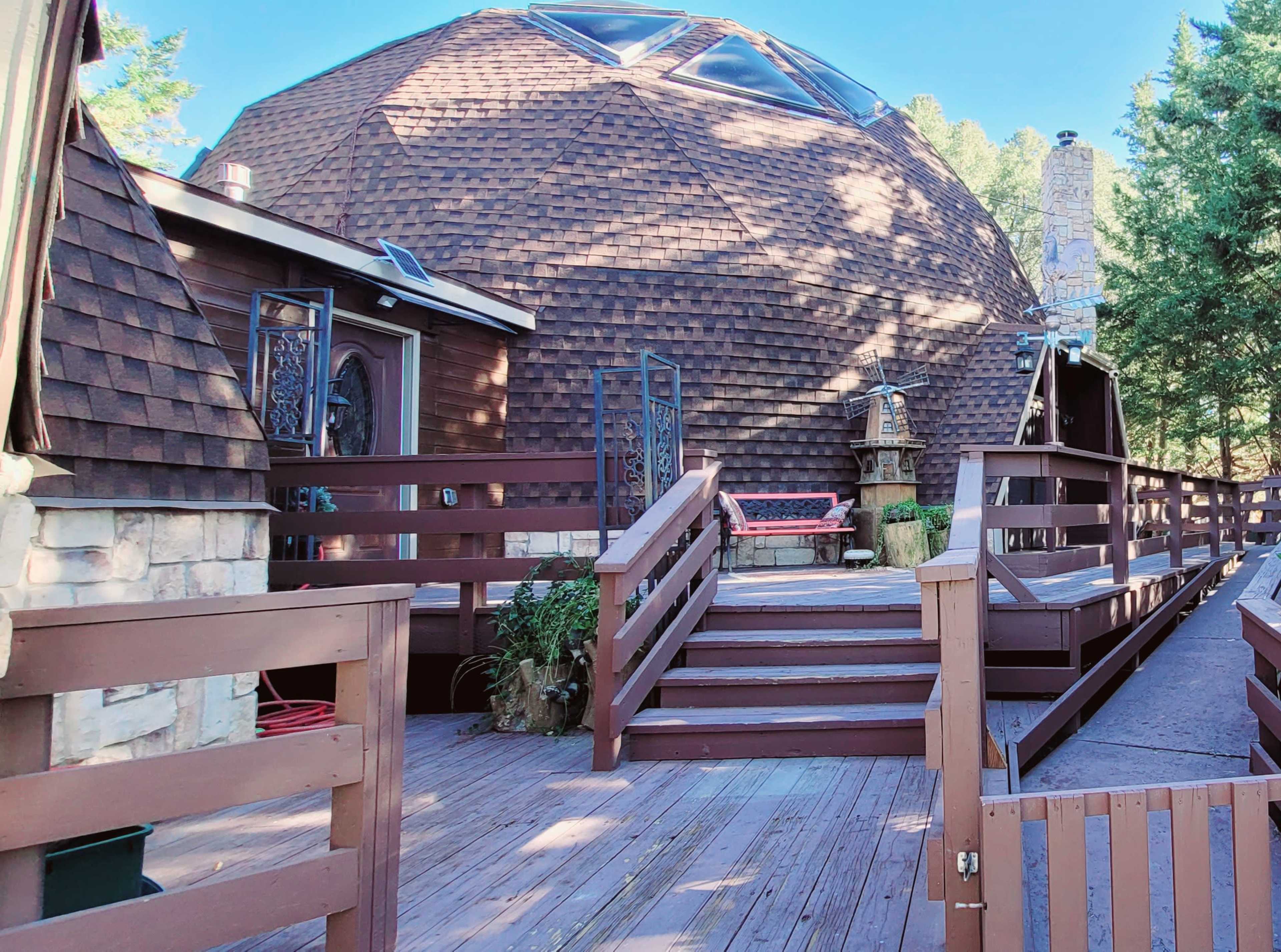 A wooden deck leading to a large, dome-shaped building with a shingled exterior and a stone chimney.