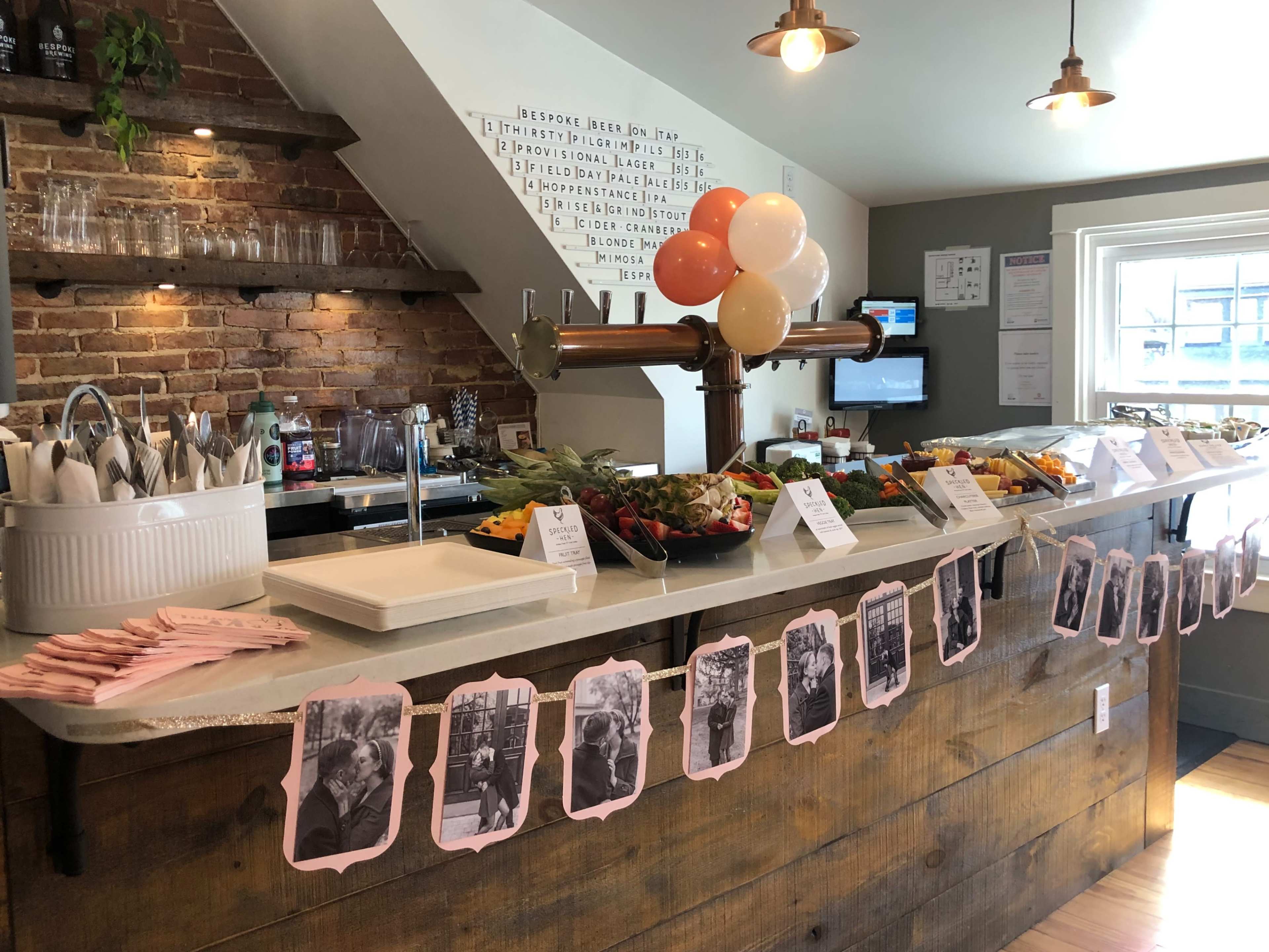 A buffet table is set up with an assortment of food and drinks, decorated with balloons and accompanied by black-and-white photographs hanging from a string.
