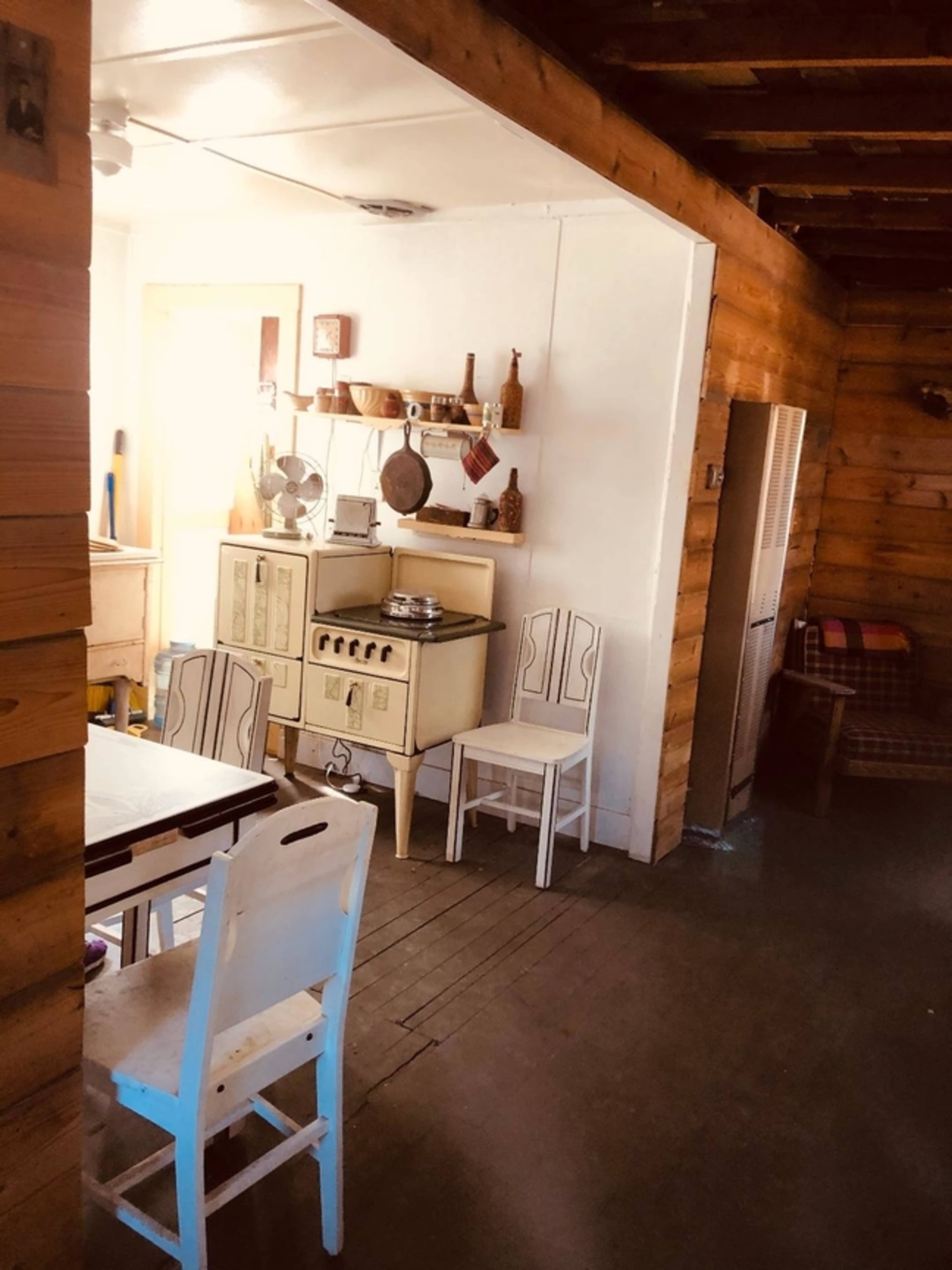 A rustic kitchen area with an old-fashioned stove, wooden walls, and a simple dining table with chairs.