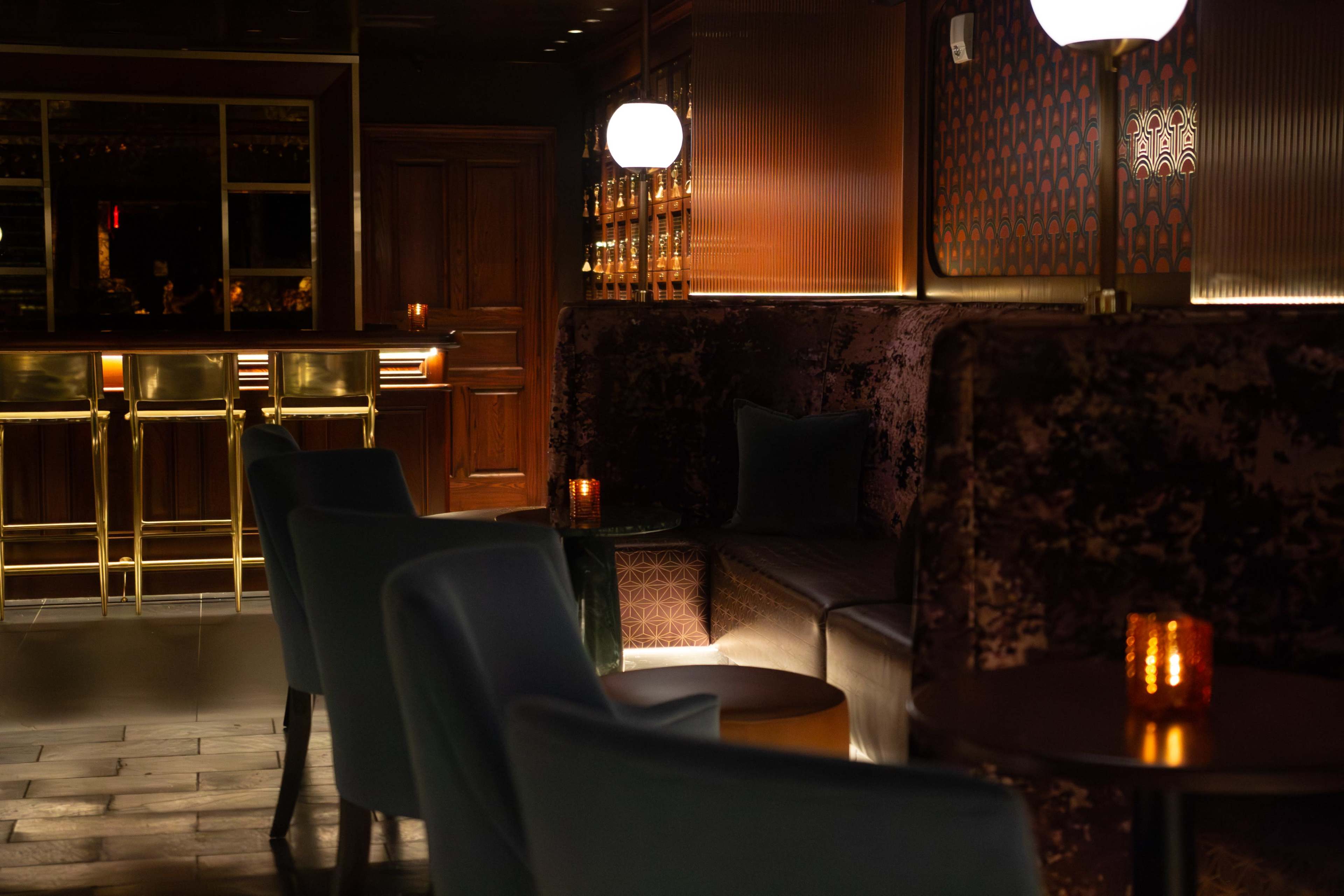 The image shows a dimly lit lounge area with plush seating, small tables, and glowing candles, creating an inviting atmosphere.
