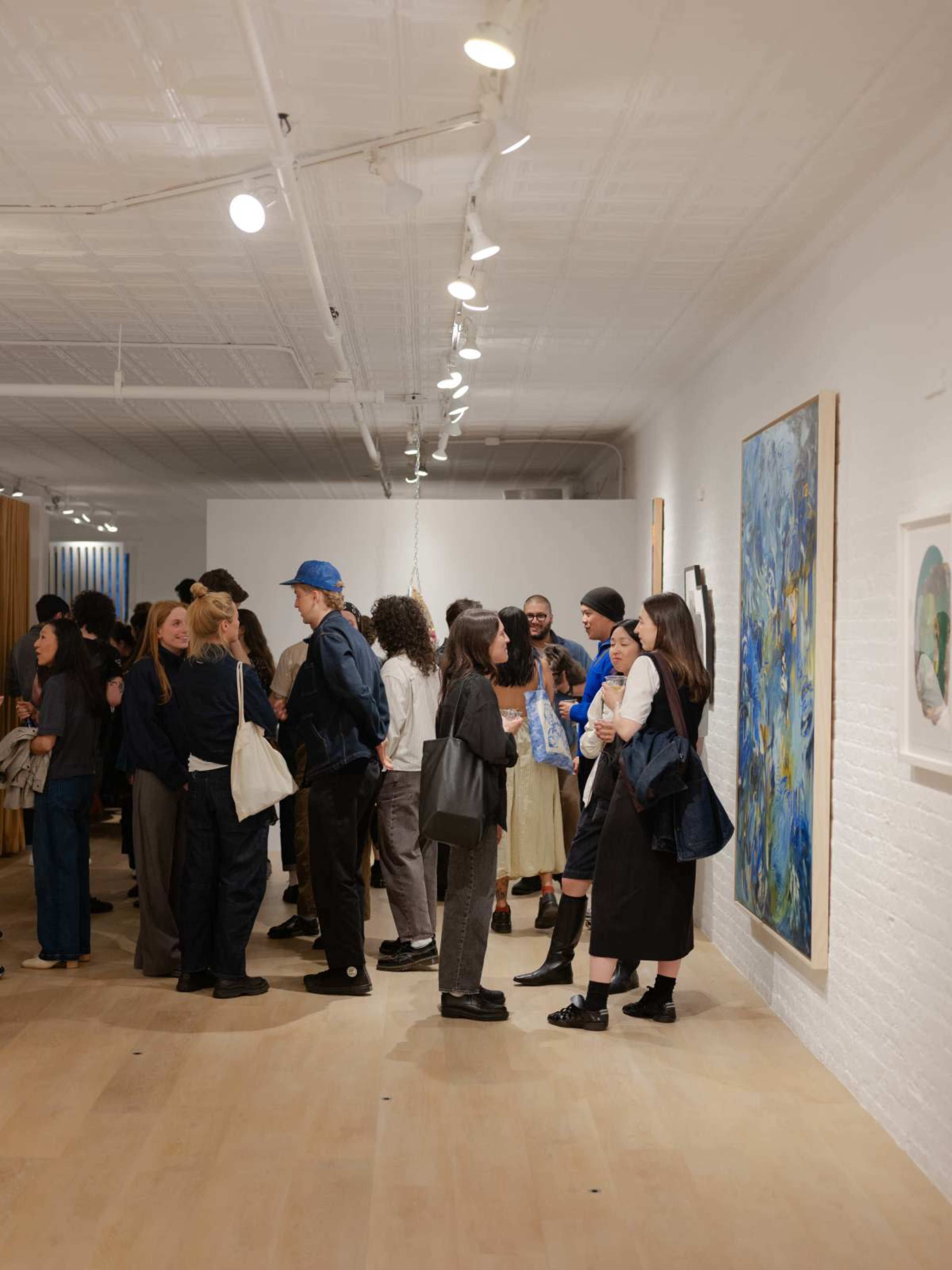 A group of people gathers in a gallery featuring colorful artworks on the walls.