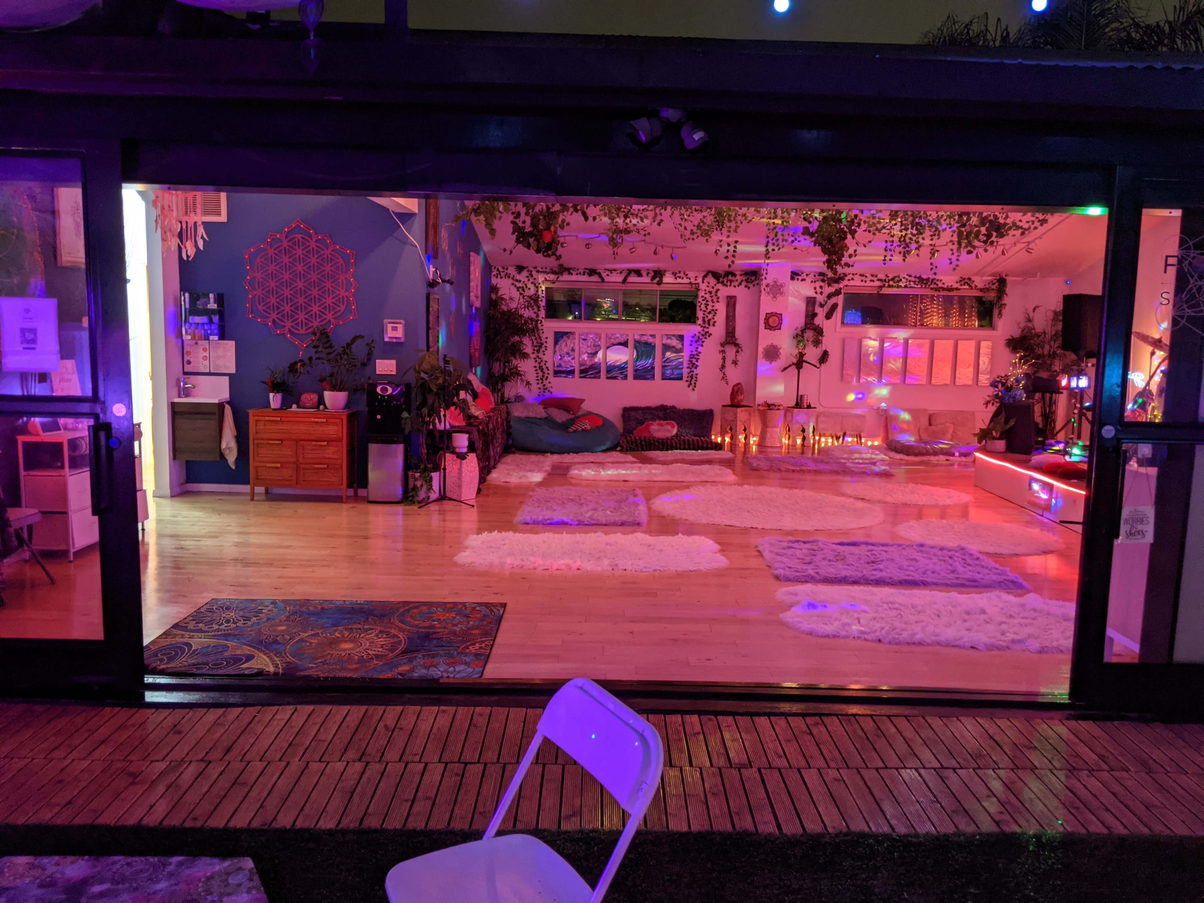 The image shows a cozy indoor space with colorful lighting, area rugs, plants, and candle arrangements, visible through large glass doors.