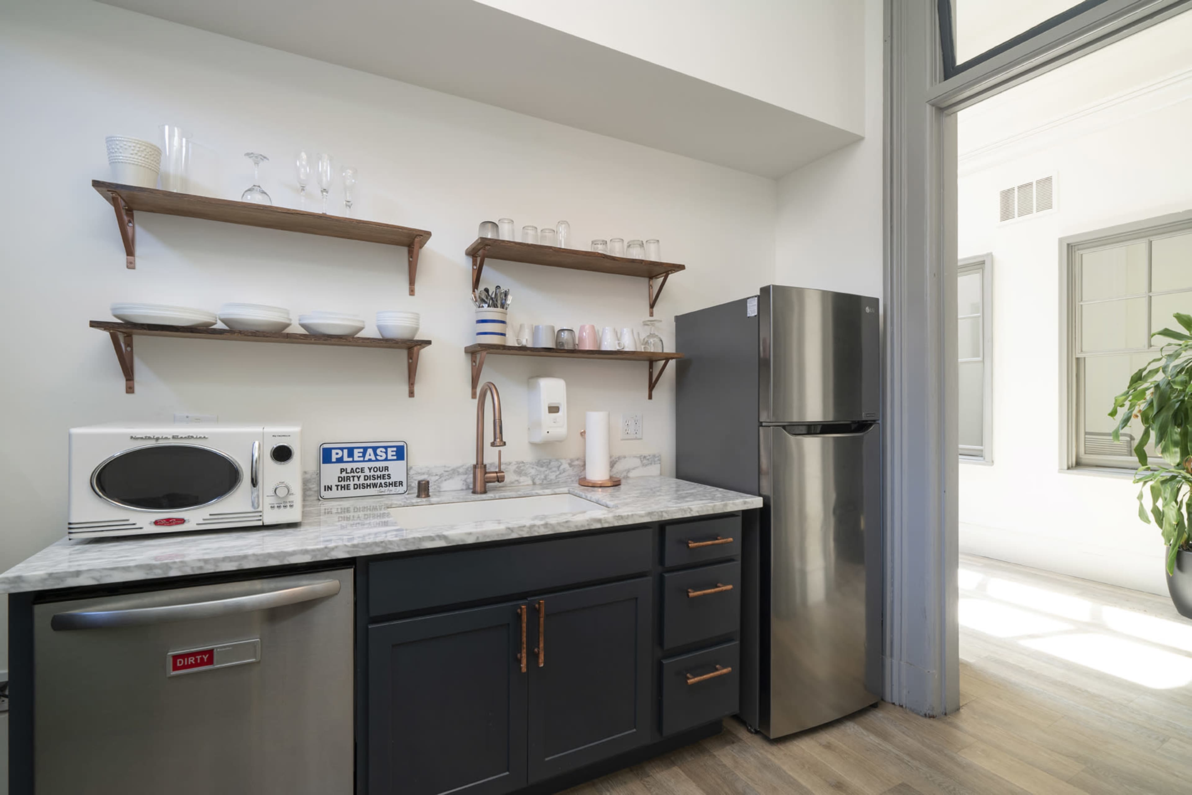 A modern kitchen area with dark cabinetry, a stainless steel refrigerator, a microwave, and open shelves displaying dishware.