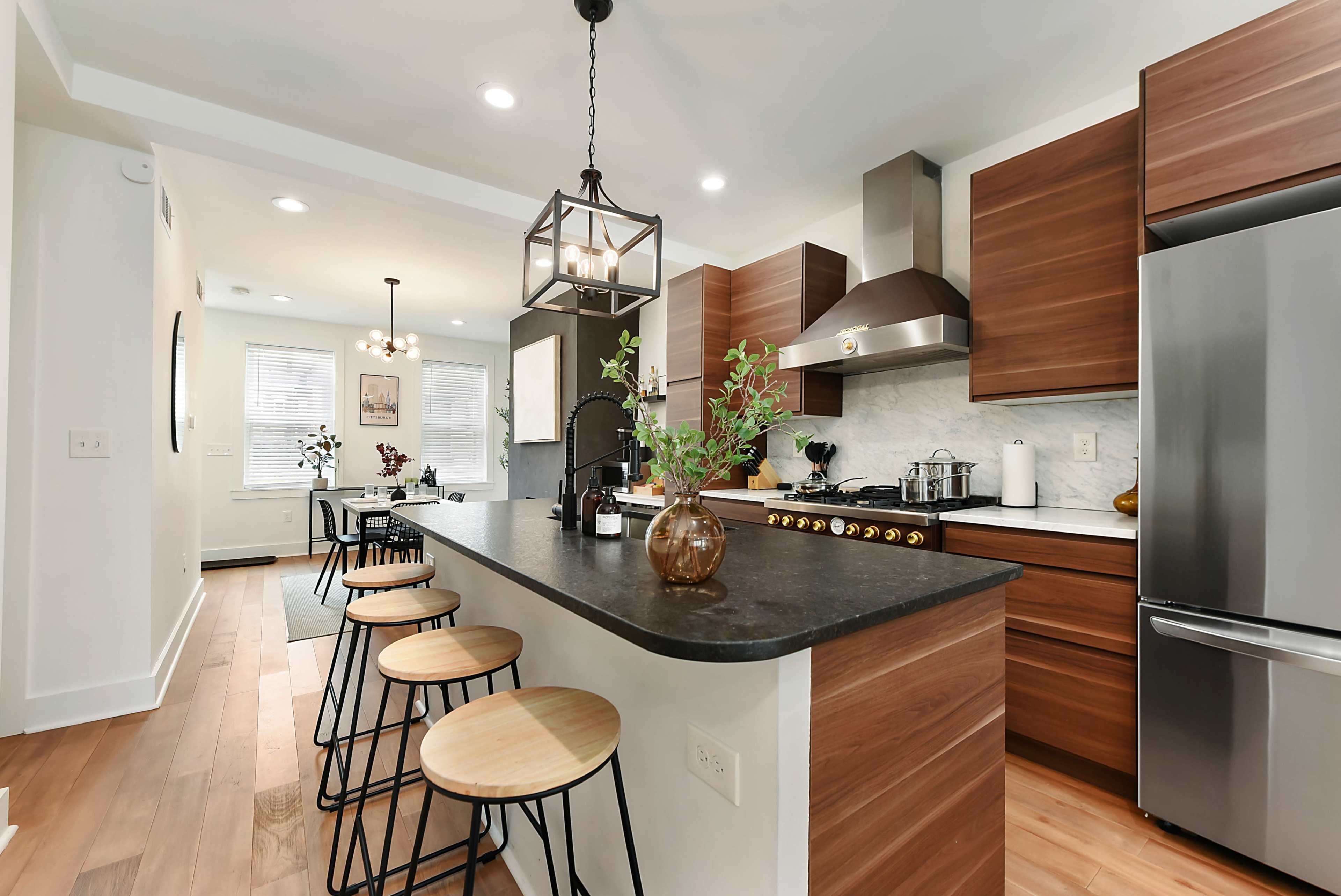 A modern kitchen features dark wooden cabinets, a large island with bar stools, and stainless steel appliances.