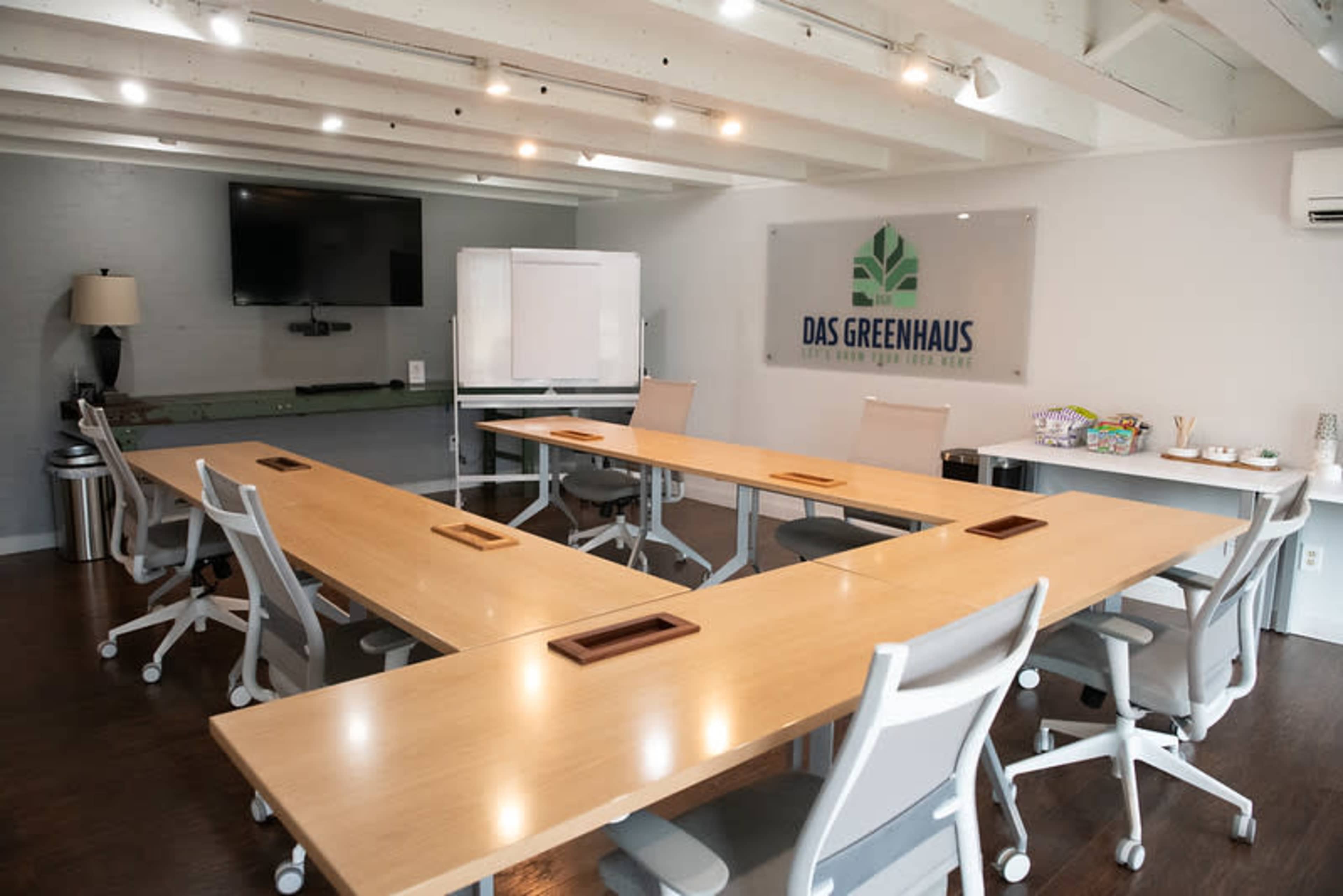 A modern conference room features a large table with multiple chairs, a wall-mounted television, and a whiteboard, all set in a well-lit space.