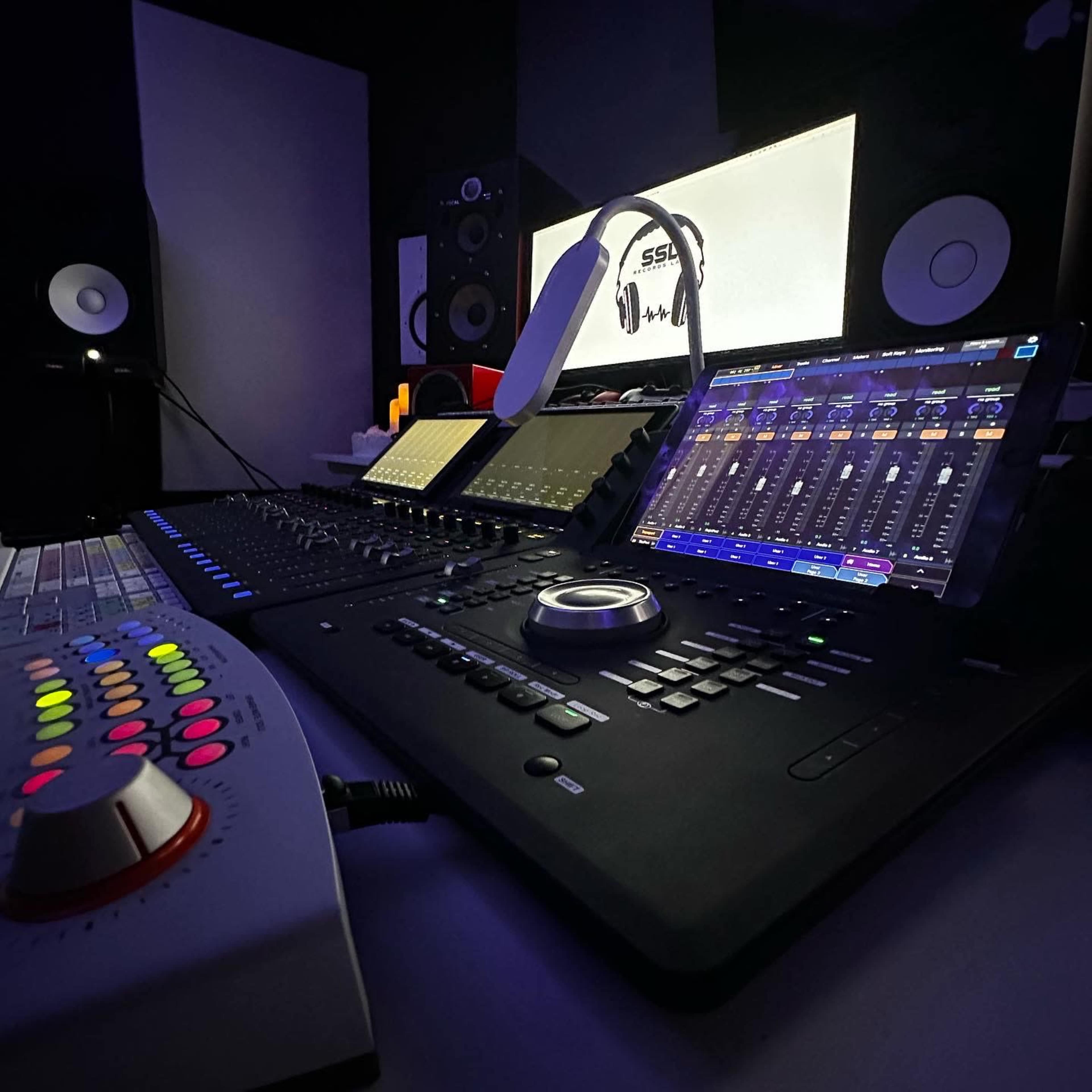 A modern music production studio setup featuring a digital mixing console, an iPad displaying audio software, and studio monitors in a dimly lit environment.