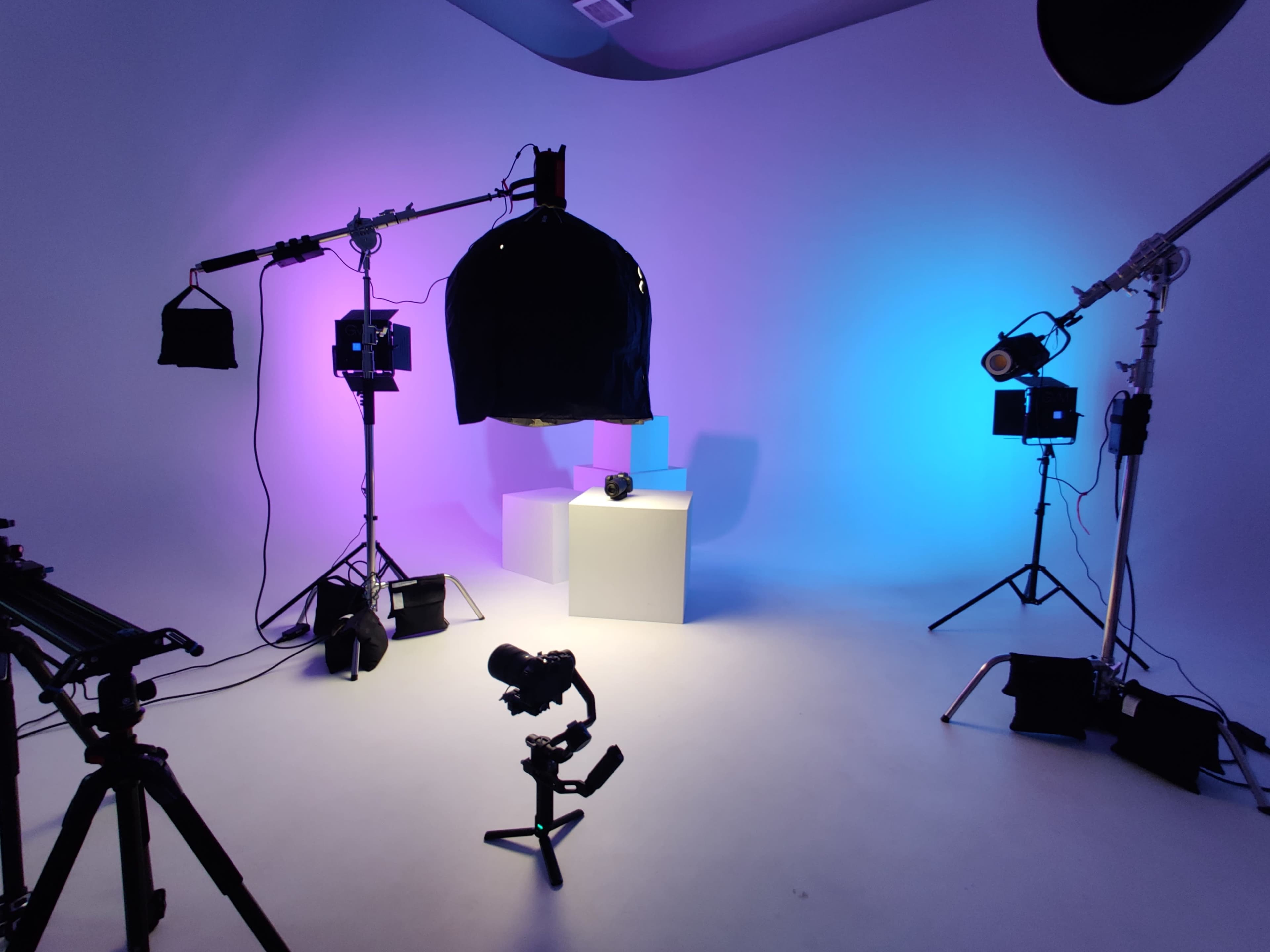 A studio setup with various lighting equipment, a black garment draped on a rack, and a white pedestal in the center.