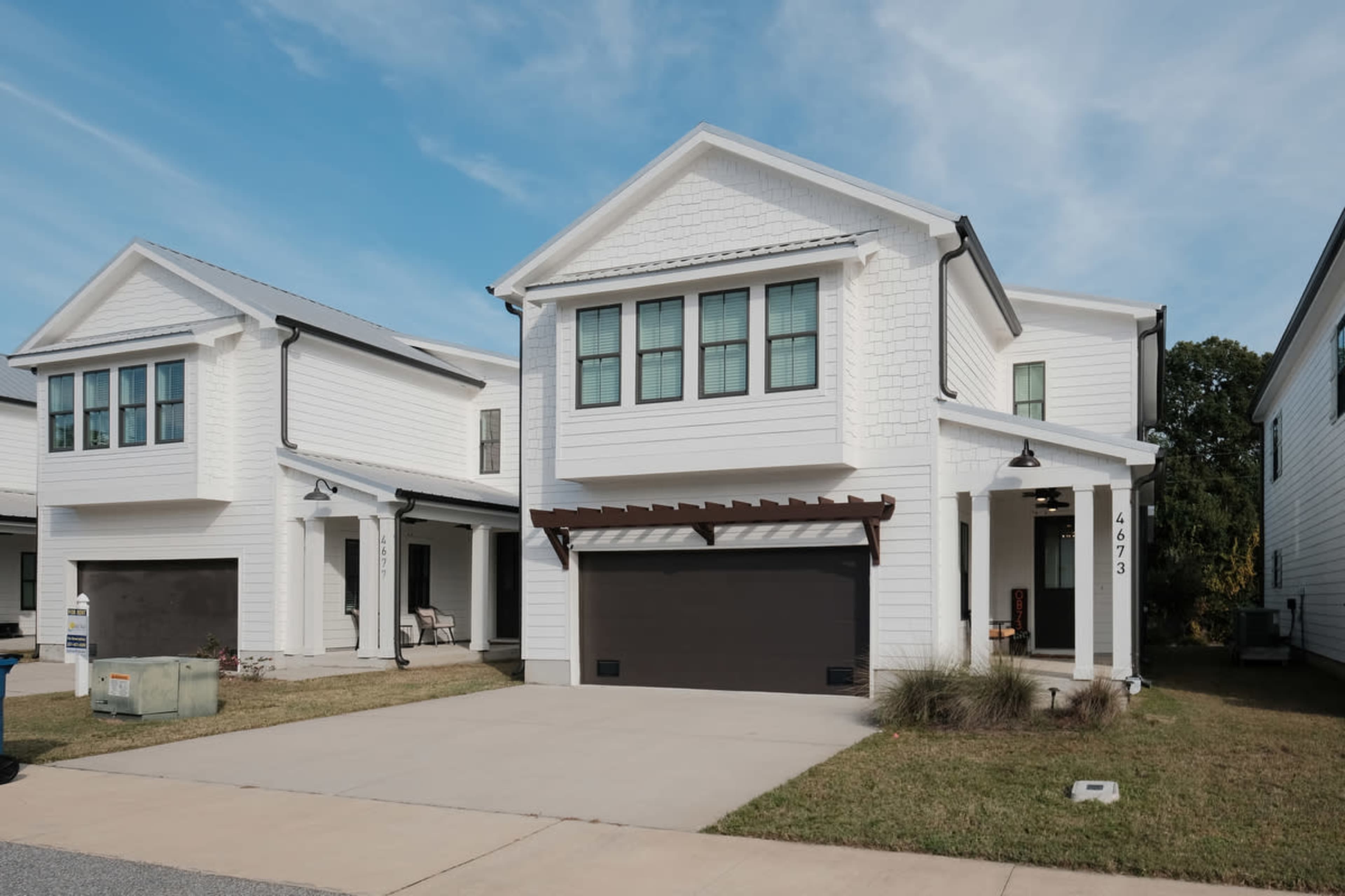 The image shows a modern two-story white house with a black garage door and a covered entrance, located in a suburban area.