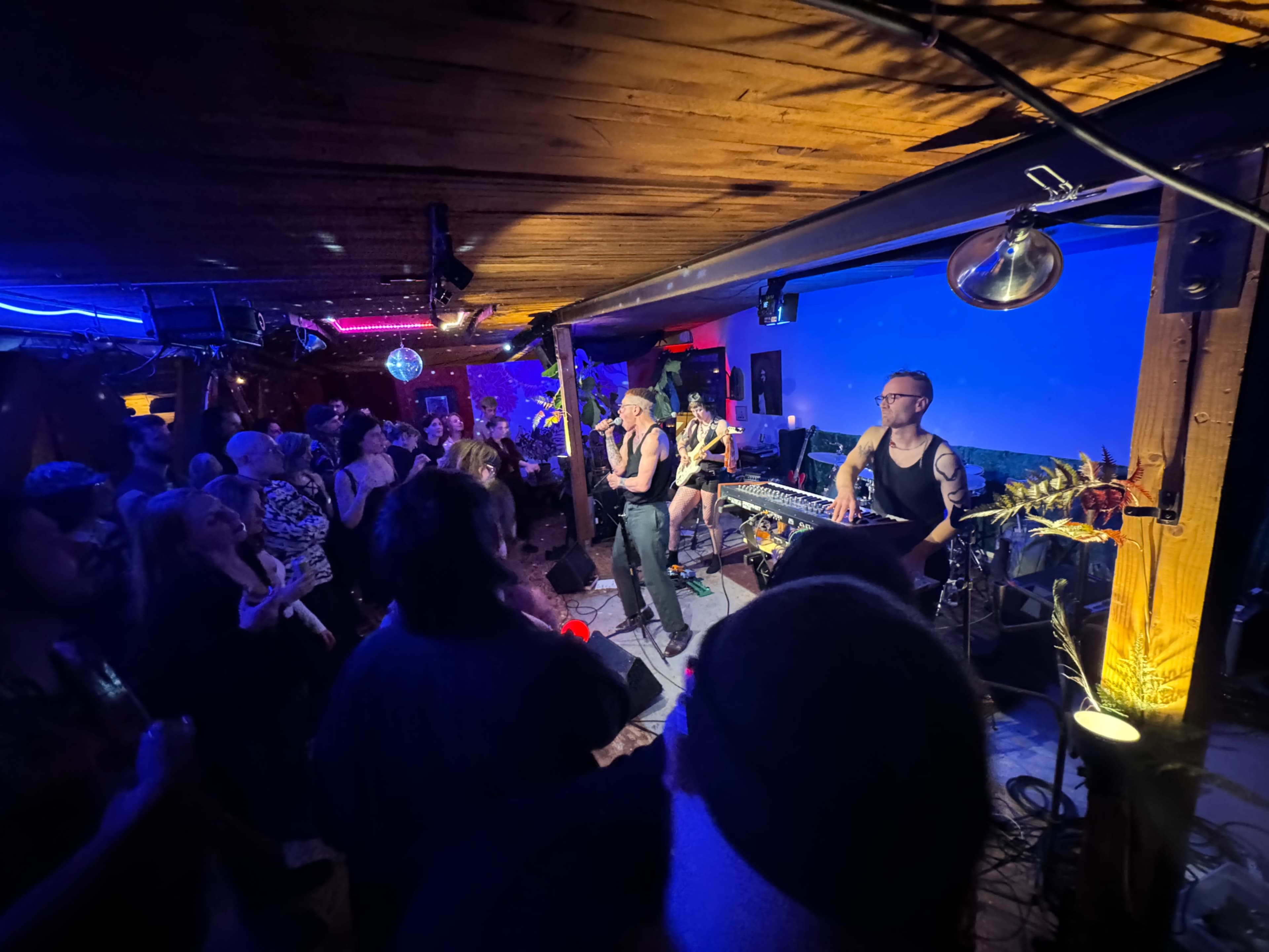 A lively music performance takes place on a stage with a small audience gathered in a dimly lit venue.