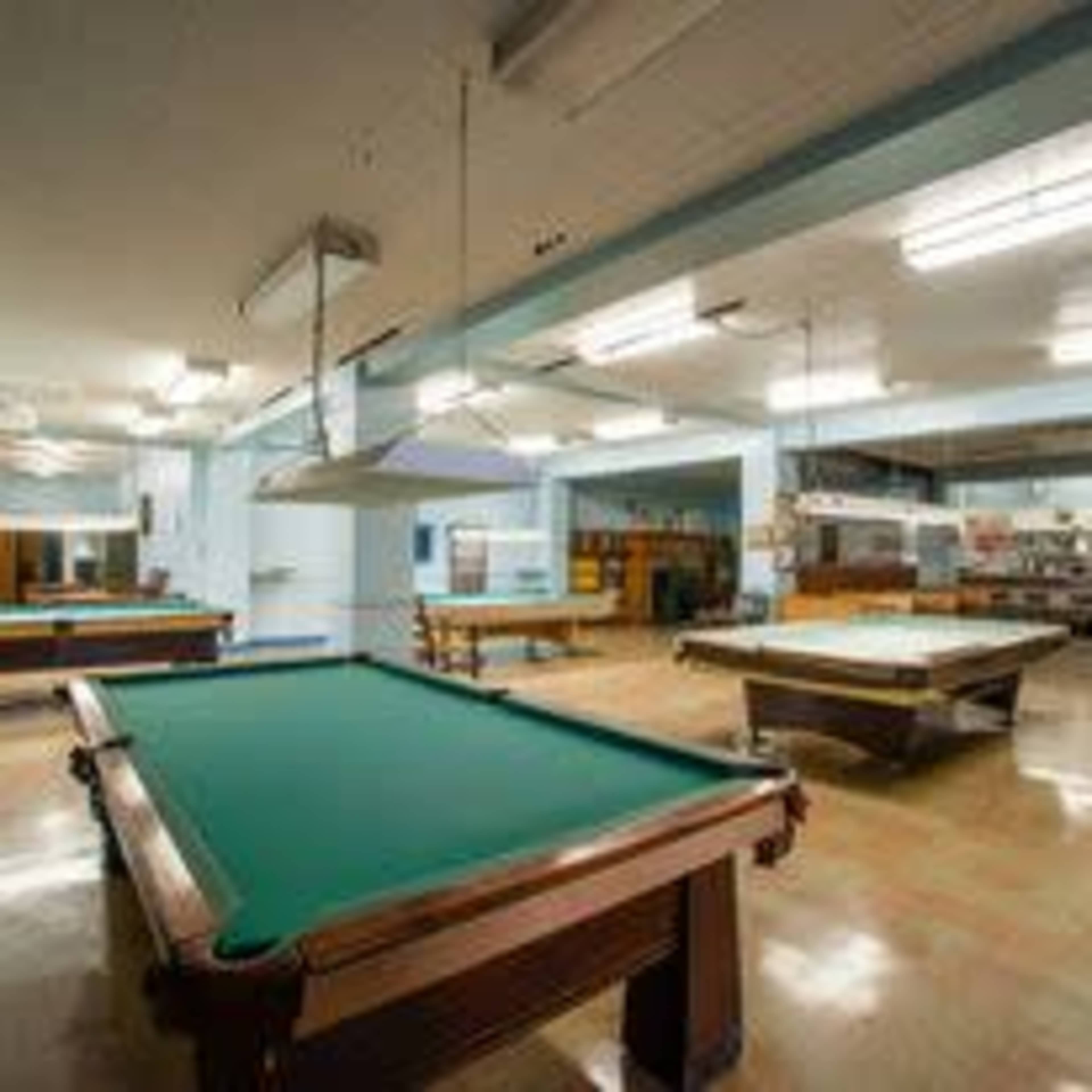 A spacious room with several pool tables arranged neatly, illuminated by overhead lights.