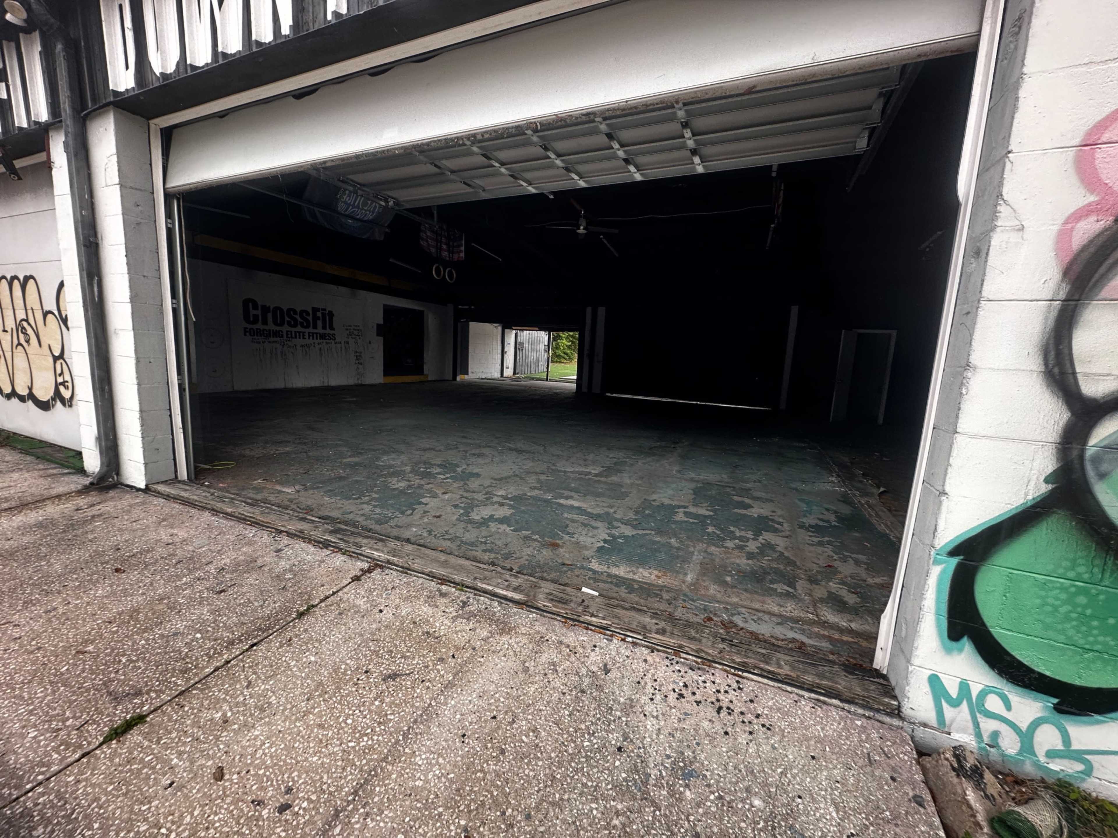 An open garage door revealing a dark, empty interior space with a worn, concrete floor.