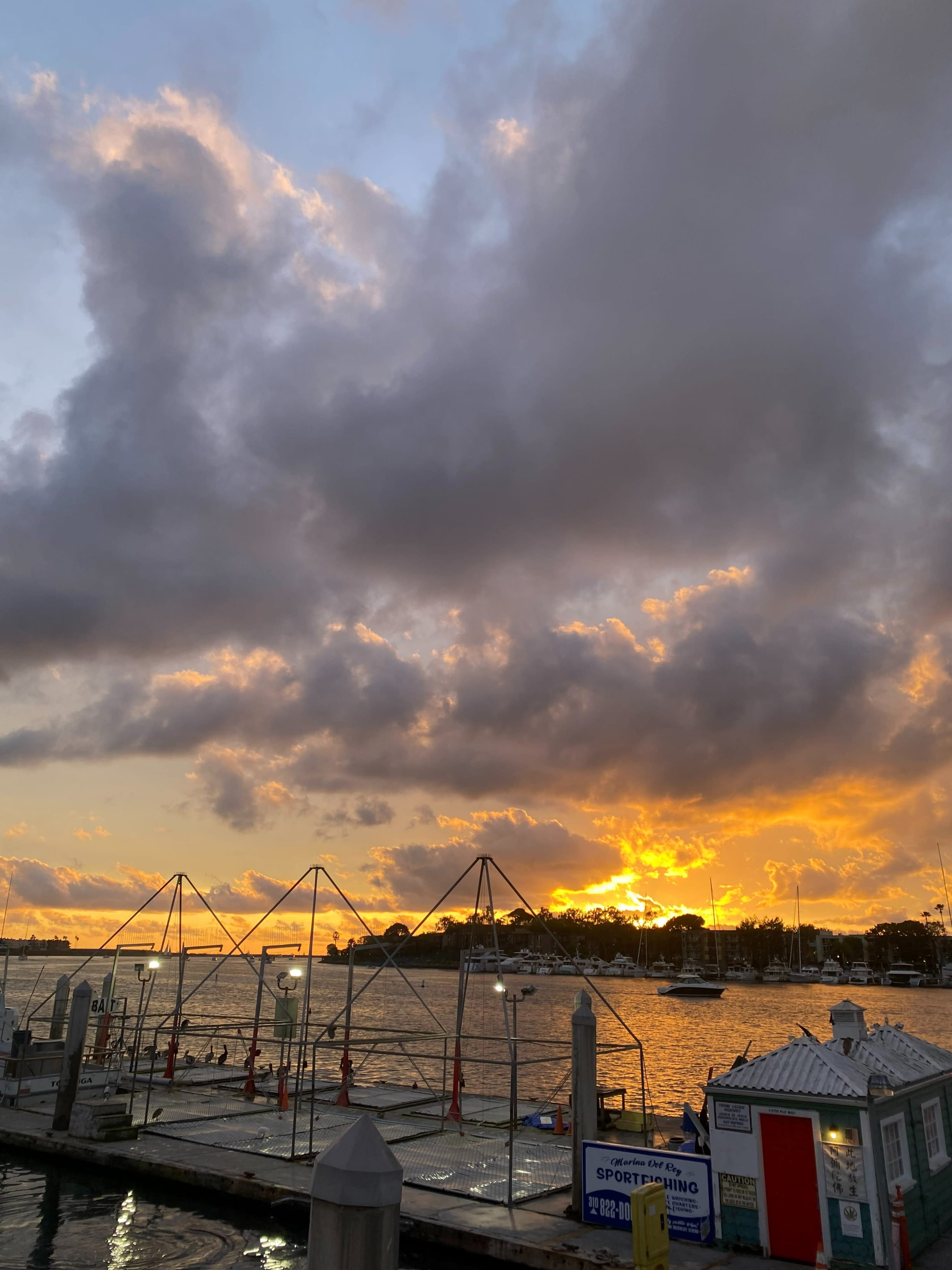 The image shows a sunset over a harbor with a dock and clouds in the sky, reflecting orange and yellow hues.
