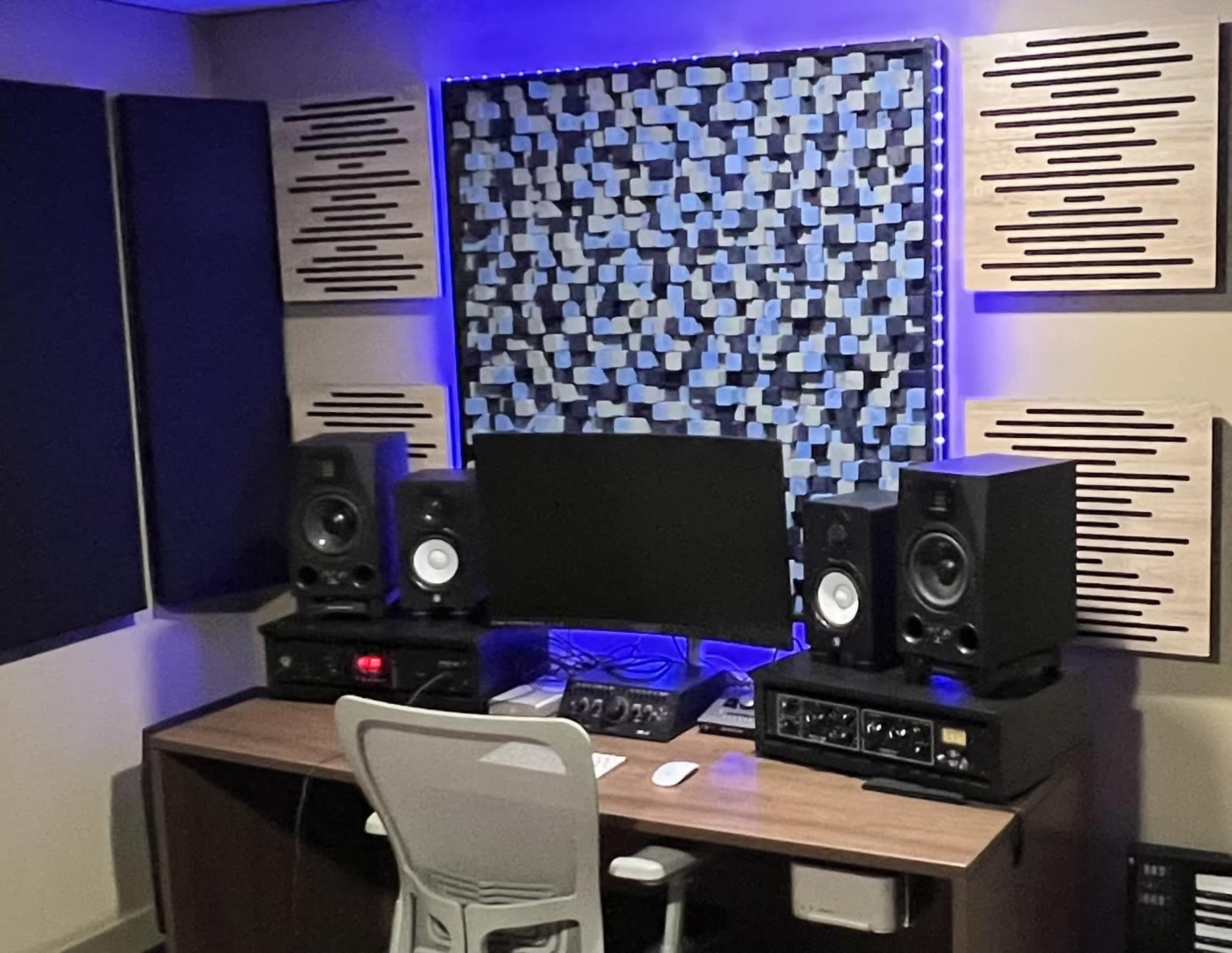 The image shows a home studio setup with a desk, a computer monitor, audio speakers, and acoustic panels on the walls.