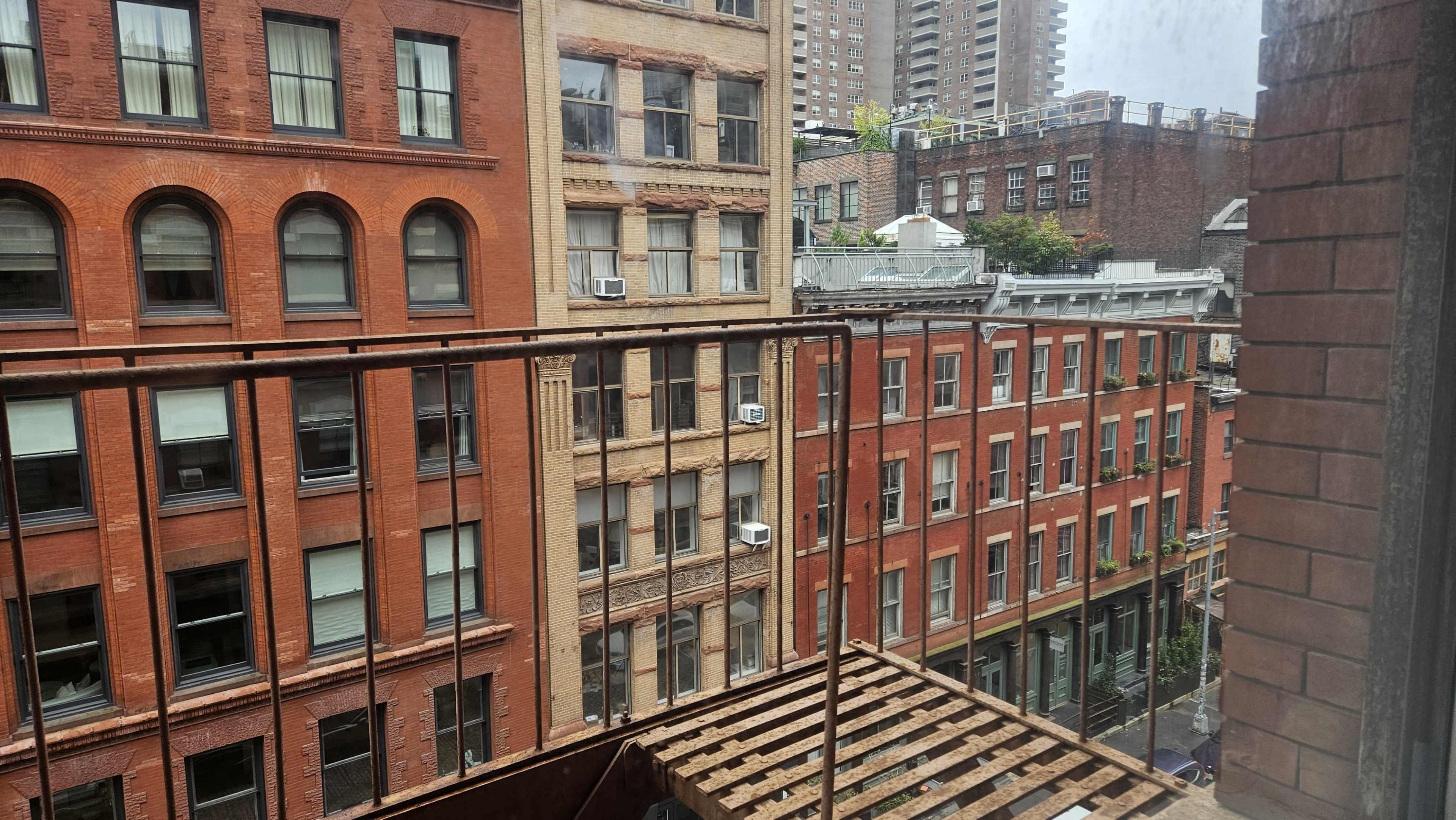 The image shows a view from a balcony showcasing a brick-lined urban landscape with buildings in various states of repair.