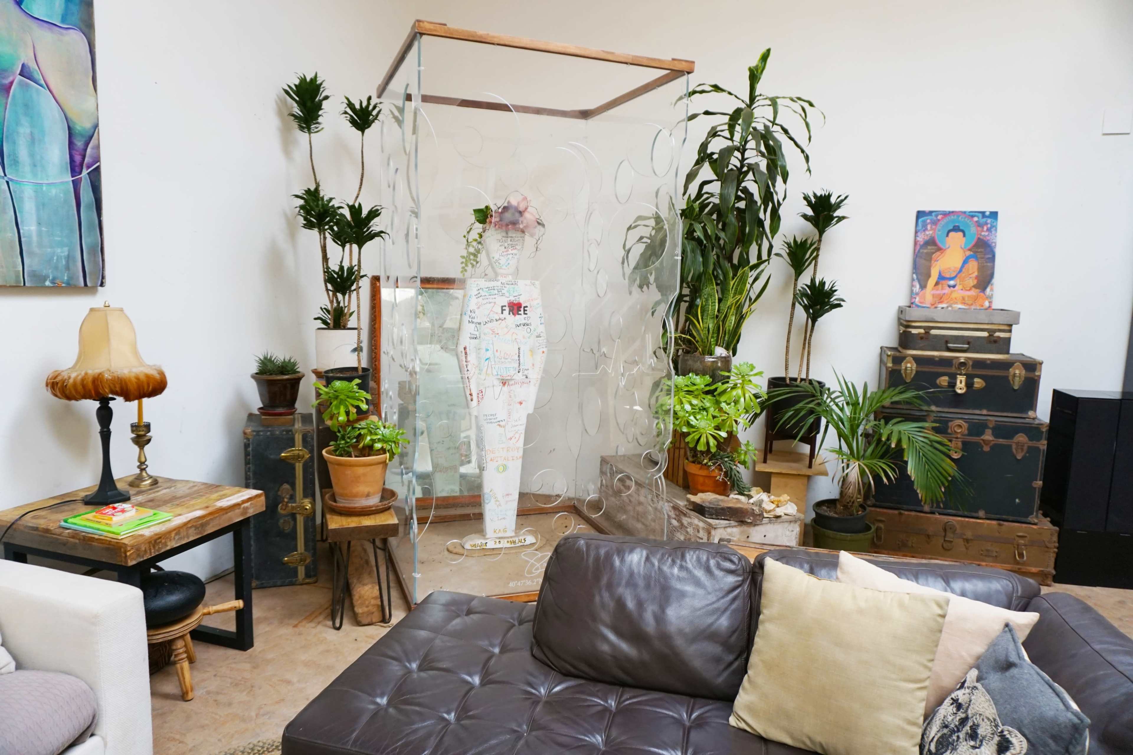 A cozy indoor space featuring a leather couch, a standing mirror surrounded by plants, and a decorative screen made of circular panels.