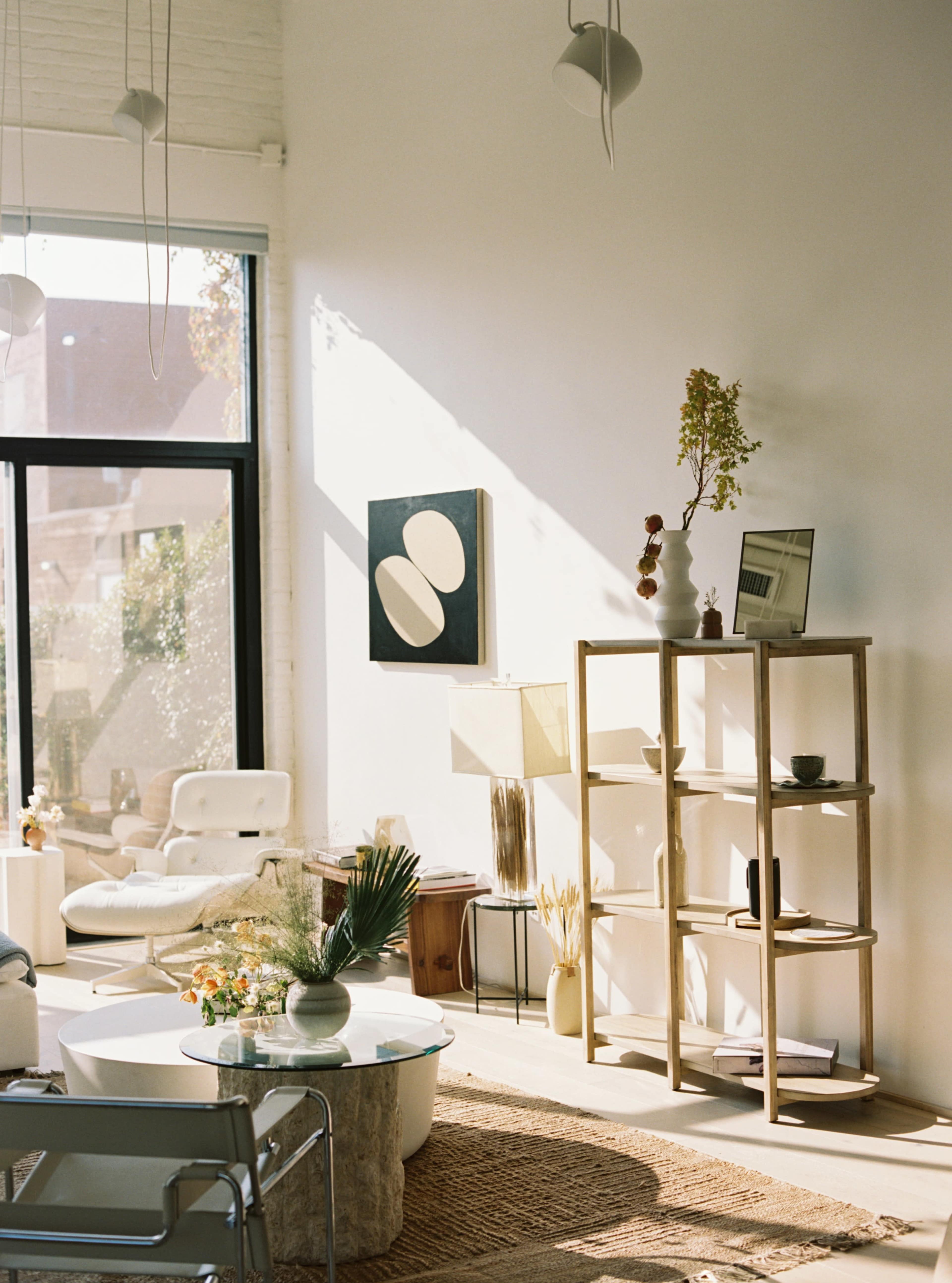 A bright living room features a modern seating area, a wooden shelving unit, and a large window allowing natural light to fill the space.