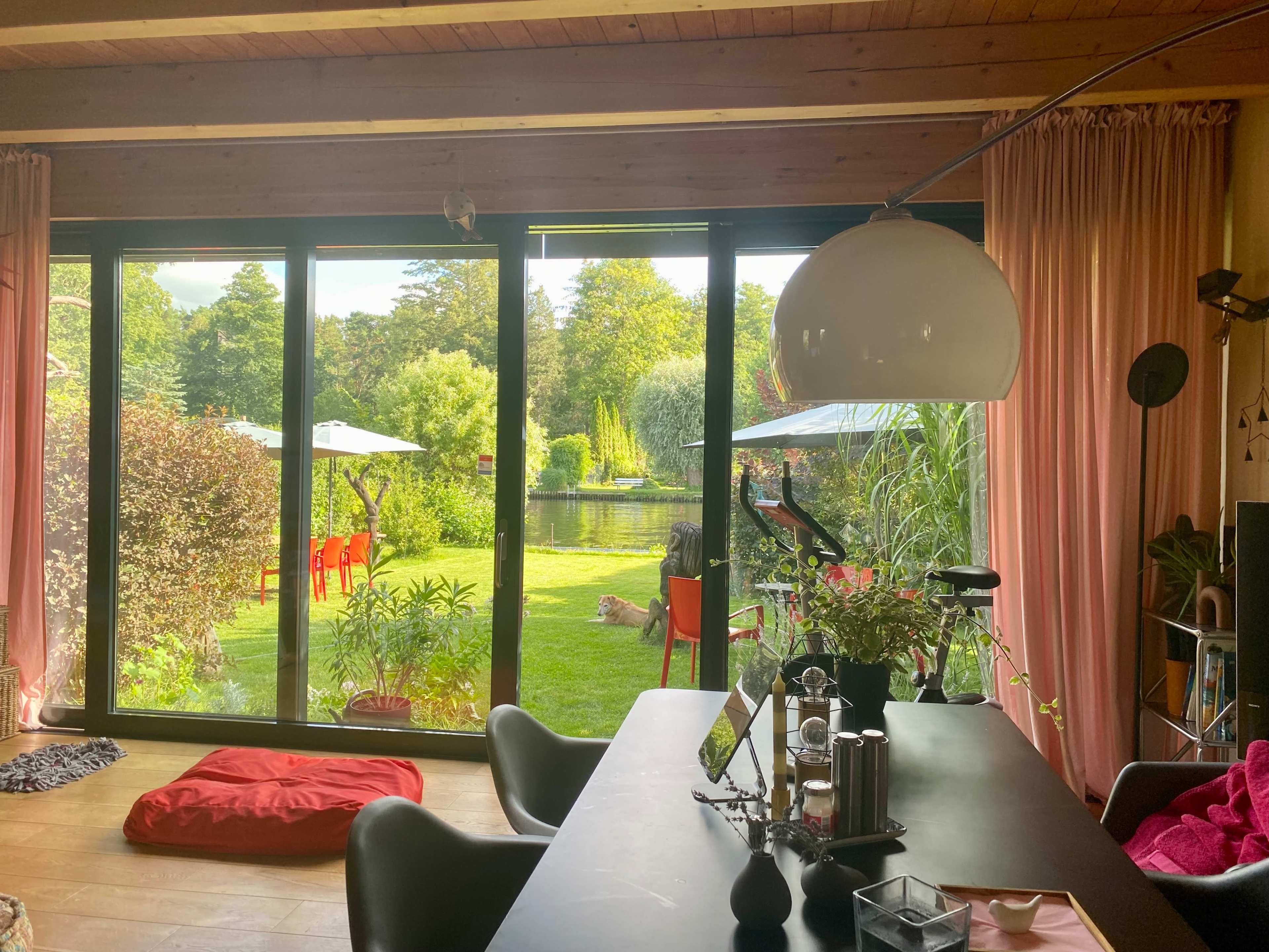 A modern interior space with large glass windows overlooking a landscaped garden featuring a pond and several red chairs.