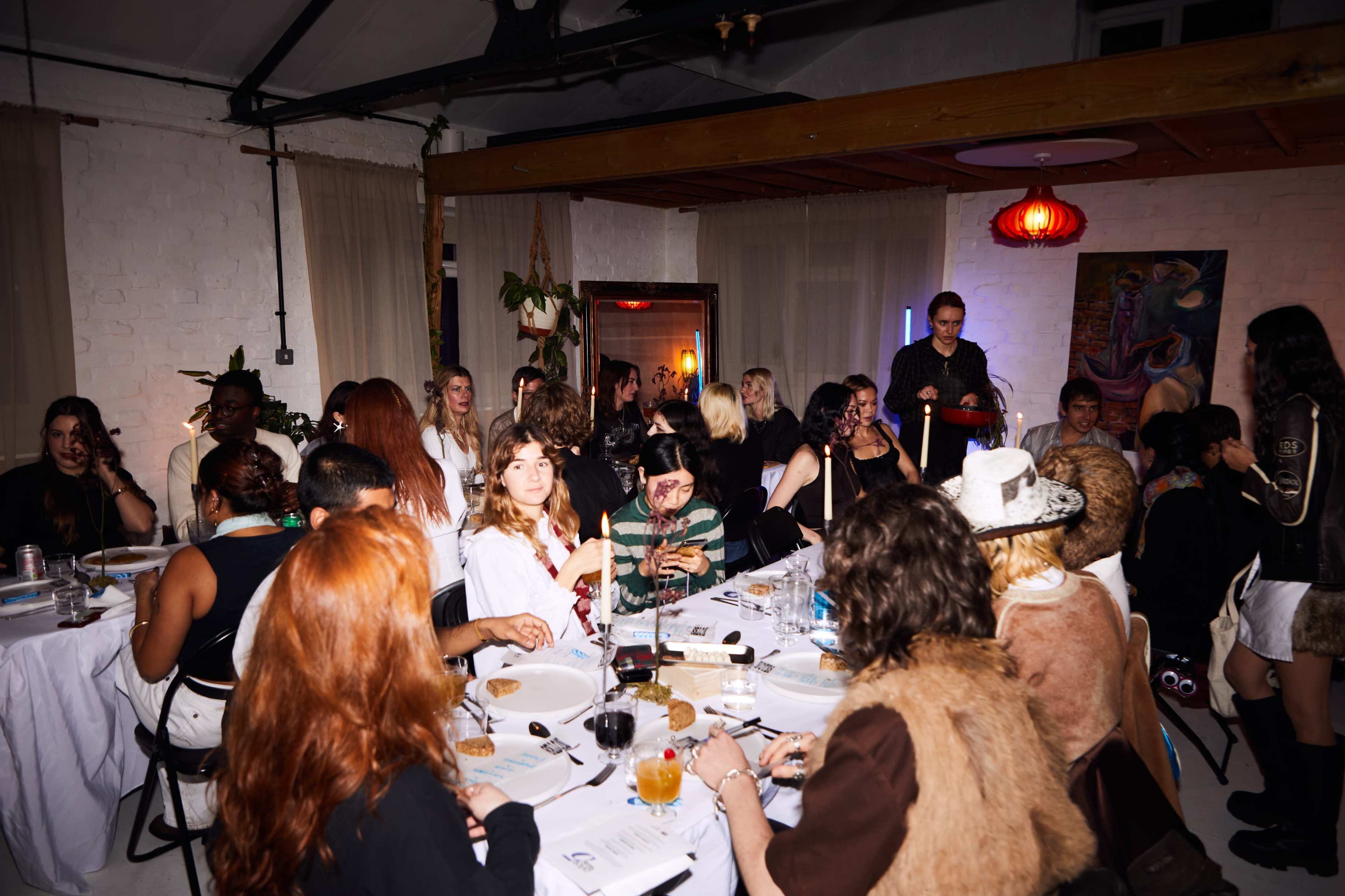 A large group of people are sitting around a long table in a well-decorated indoor space with a variety of dishes and drinks.