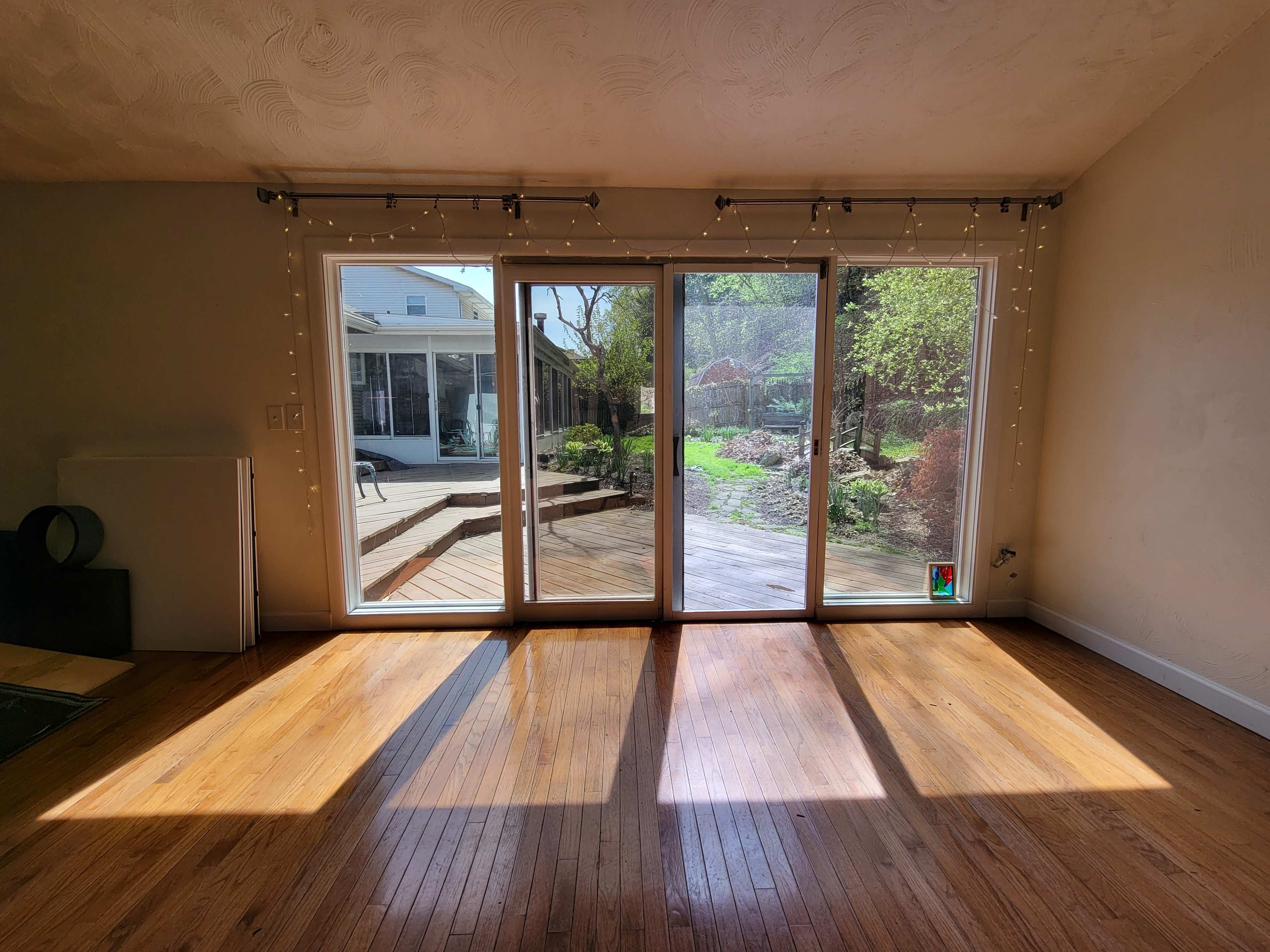 The image shows a brightly lit room with a large sliding glass door leading to a wooden deck and an outdoor garden area.
