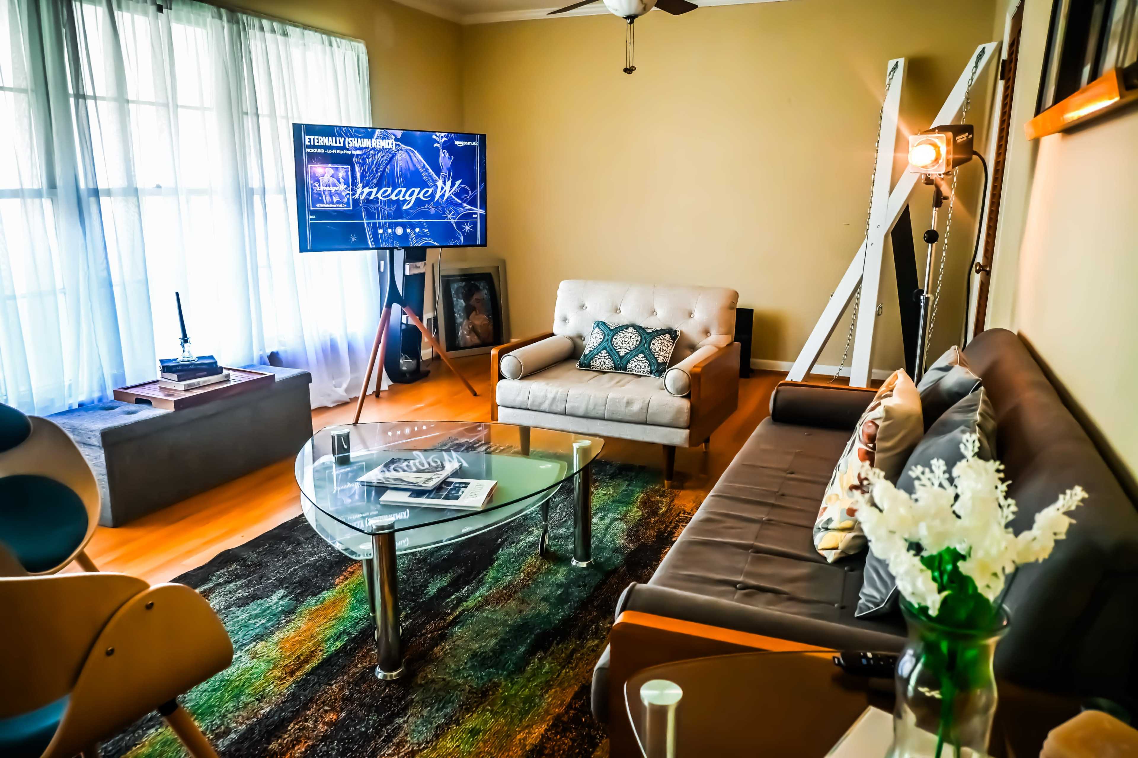 The living room features a comfortable seating area with two sofas, a coffee table, a television, and large windows allowing natural light to enter.