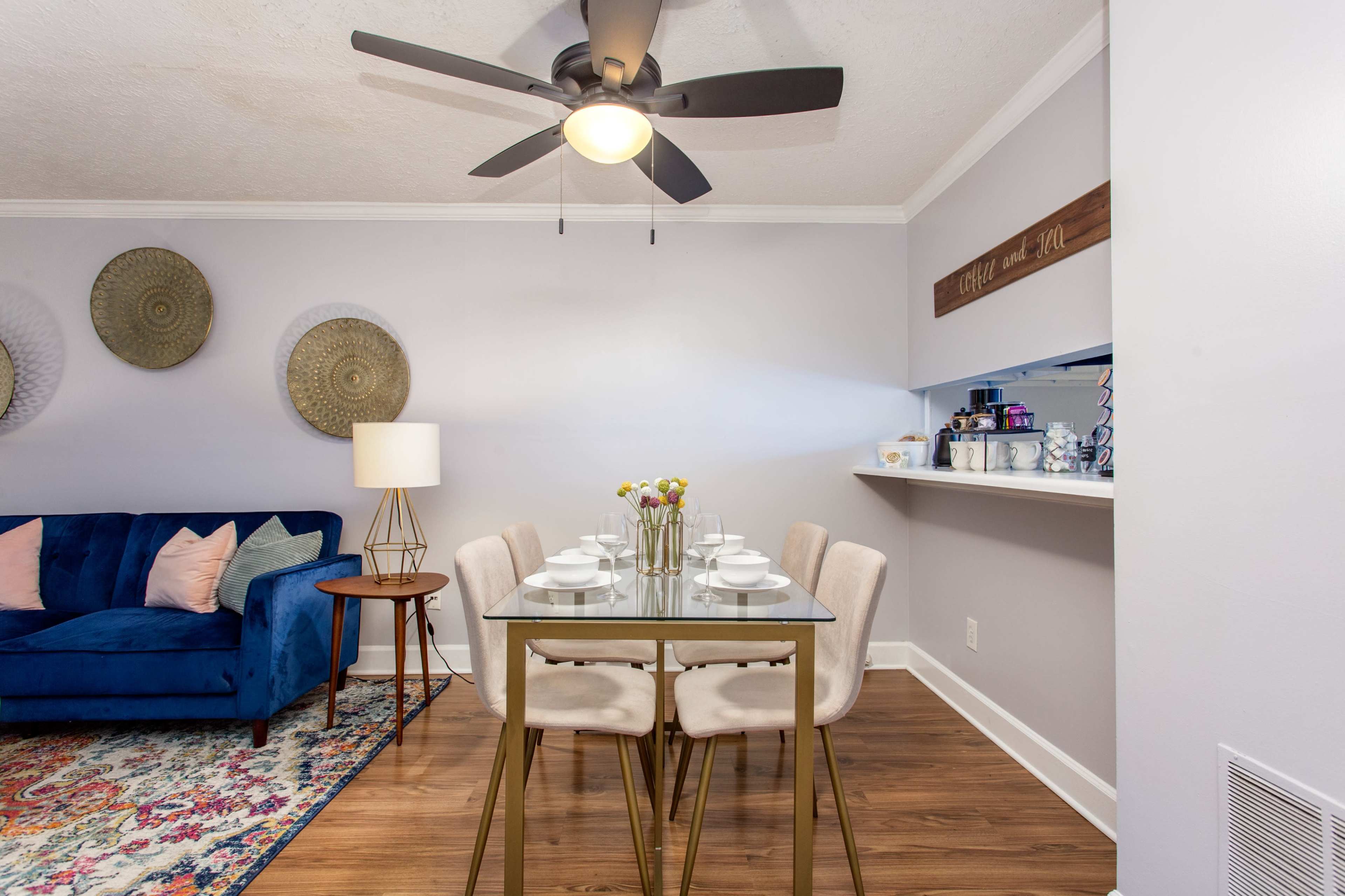 A modern dining area with a table set for four, a blue sofa to the left, and decorative wall elements.