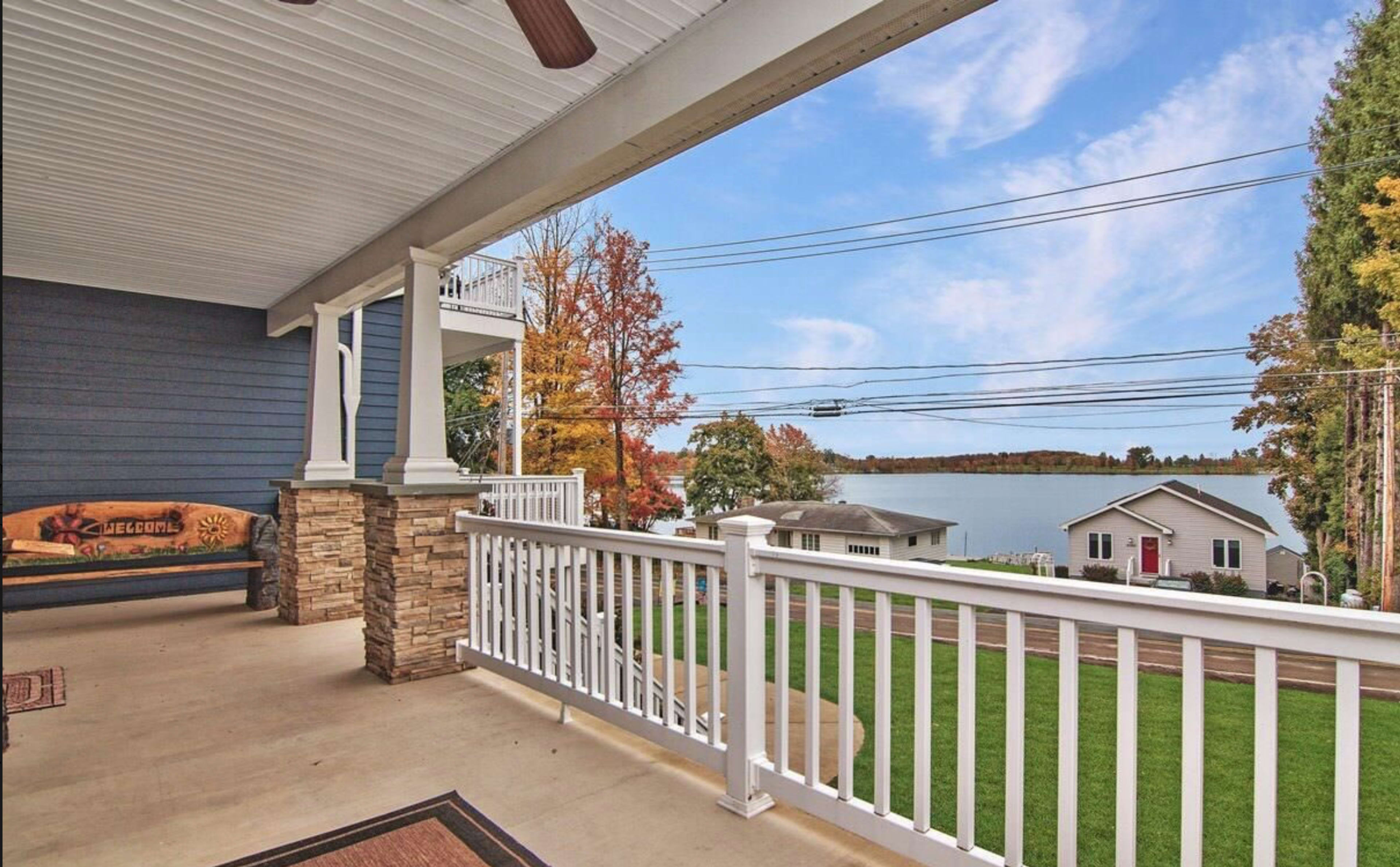 A covered porch with a stone column overlooking a lake and trees with colorful autumn foliage.