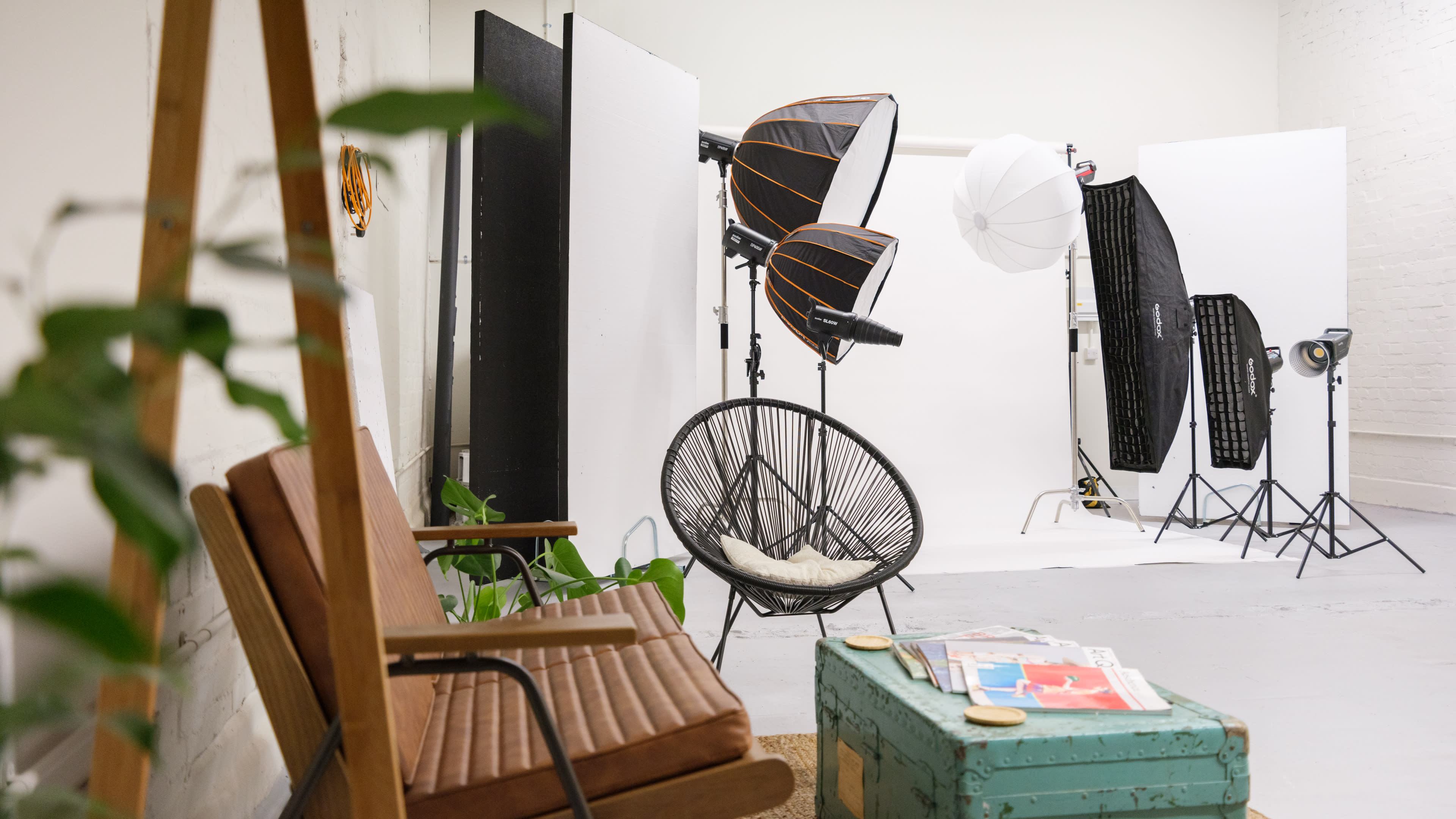 A photography studio setup featuring various lighting equipment, a green plant, and a vintage chair with a colorful storage box.