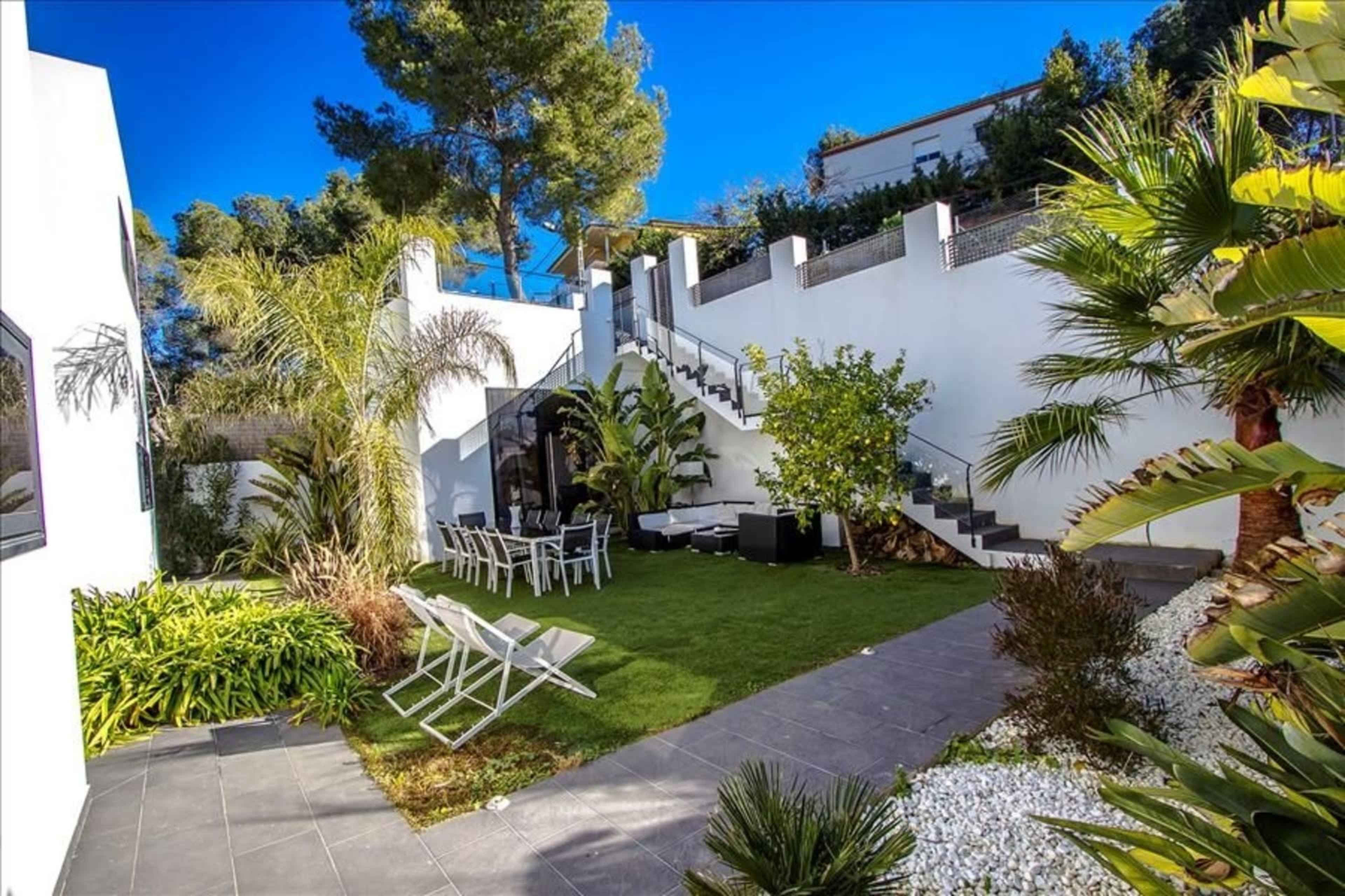 A modern garden area featuring a staircase, patio furniture, palm trees, and well-maintained greenery.