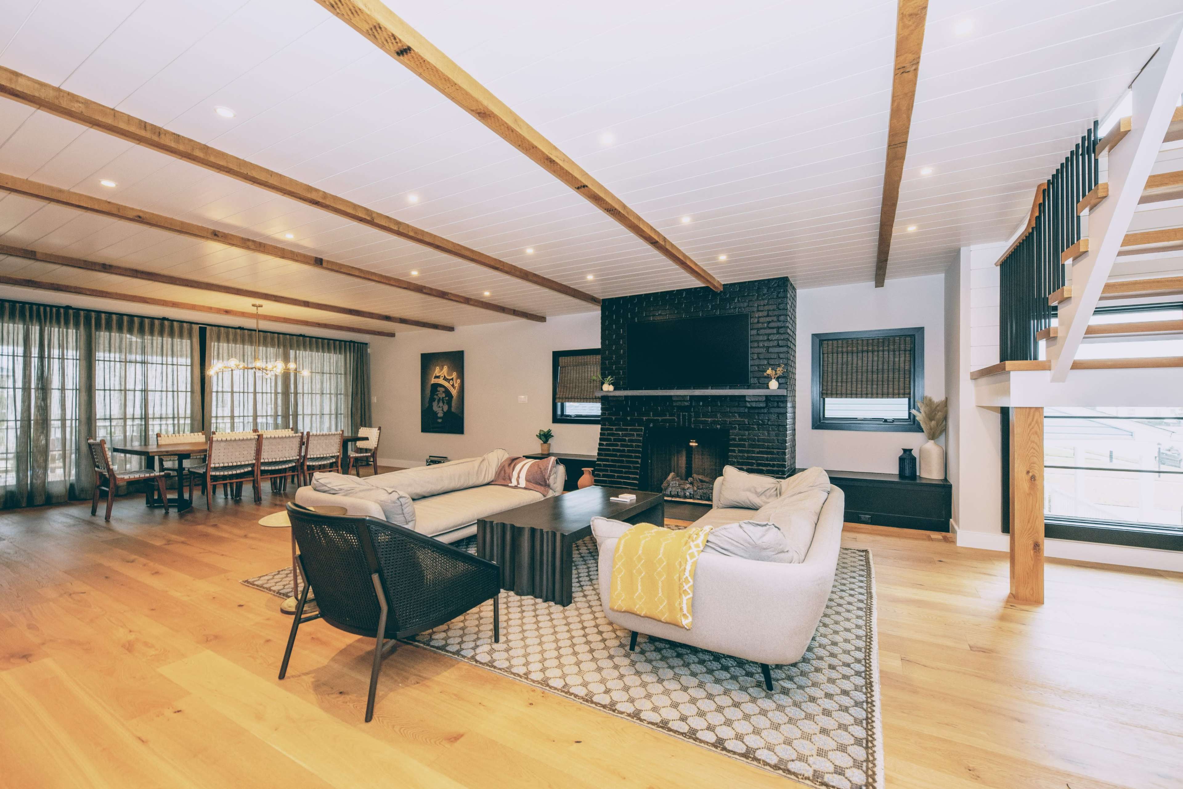 A spacious modern living room with hardwood flooring, a large sectional sofa, a fireplace, and a dining area in the background.