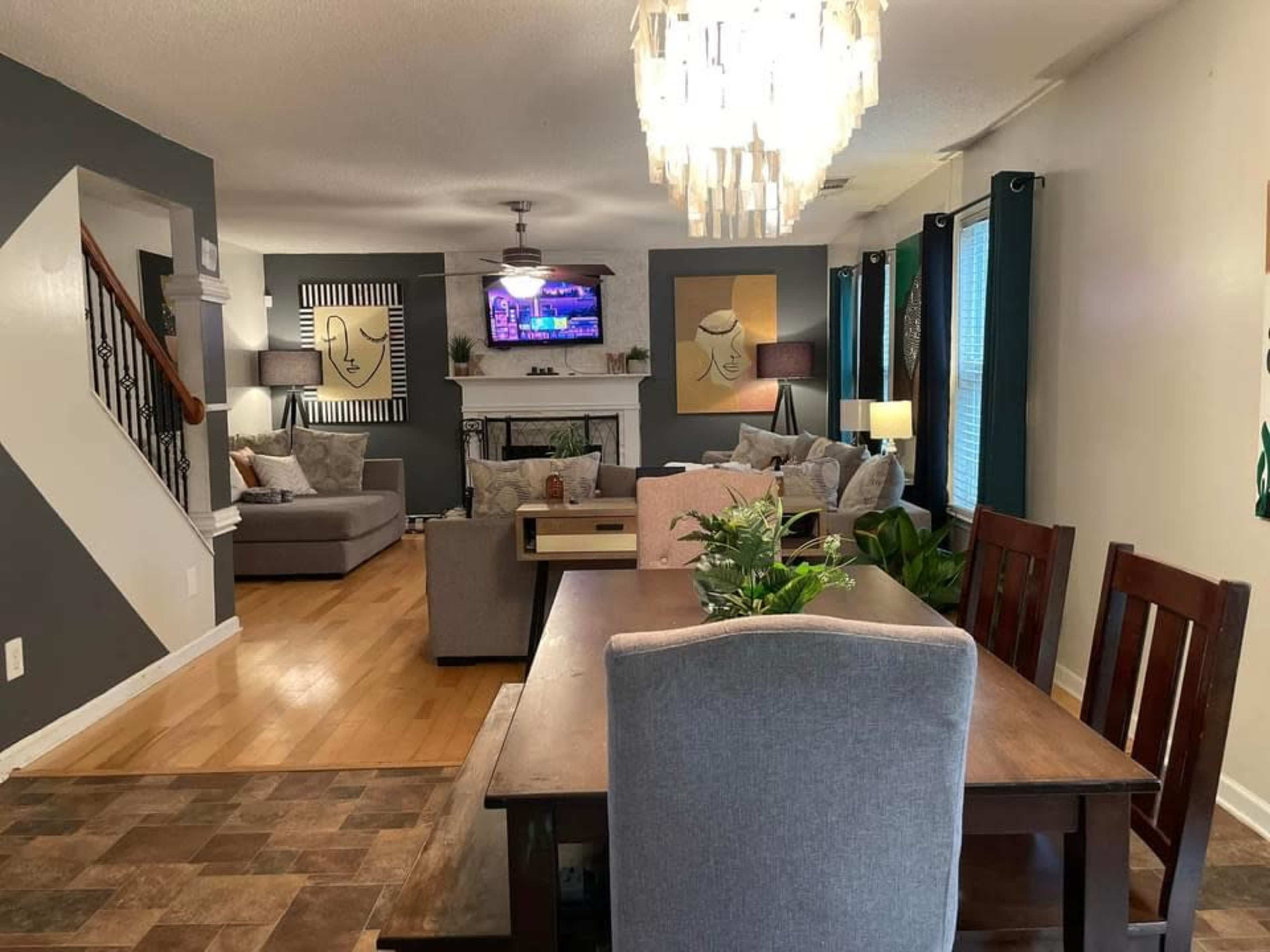 A well-lit living and dining area featuring a dining table, a sofa, a television mounted on the wall, and decorative artwork.