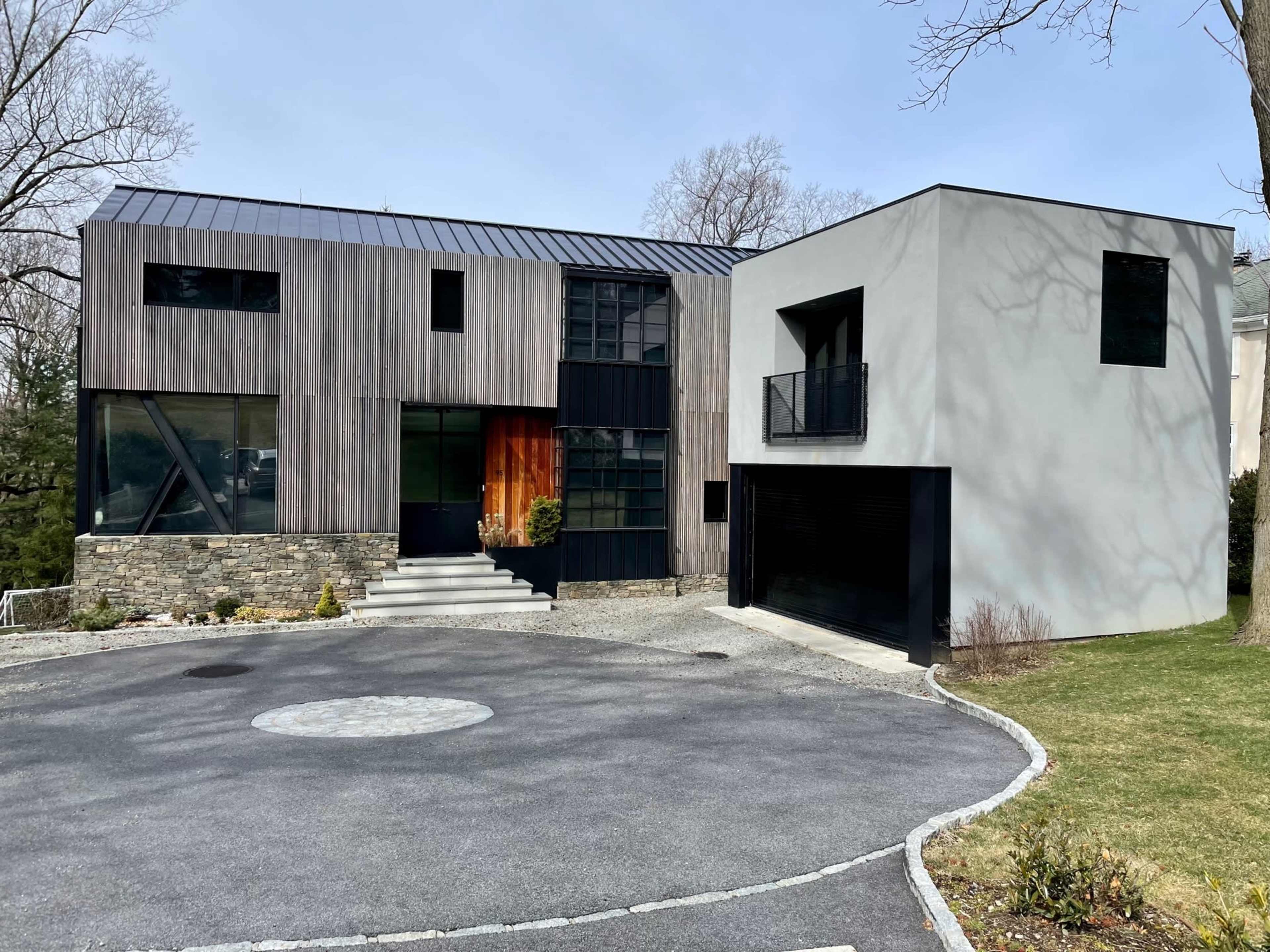 A modern house with a combination of wooden and concrete exteriors, featuring large windows and a landscaped driveway.