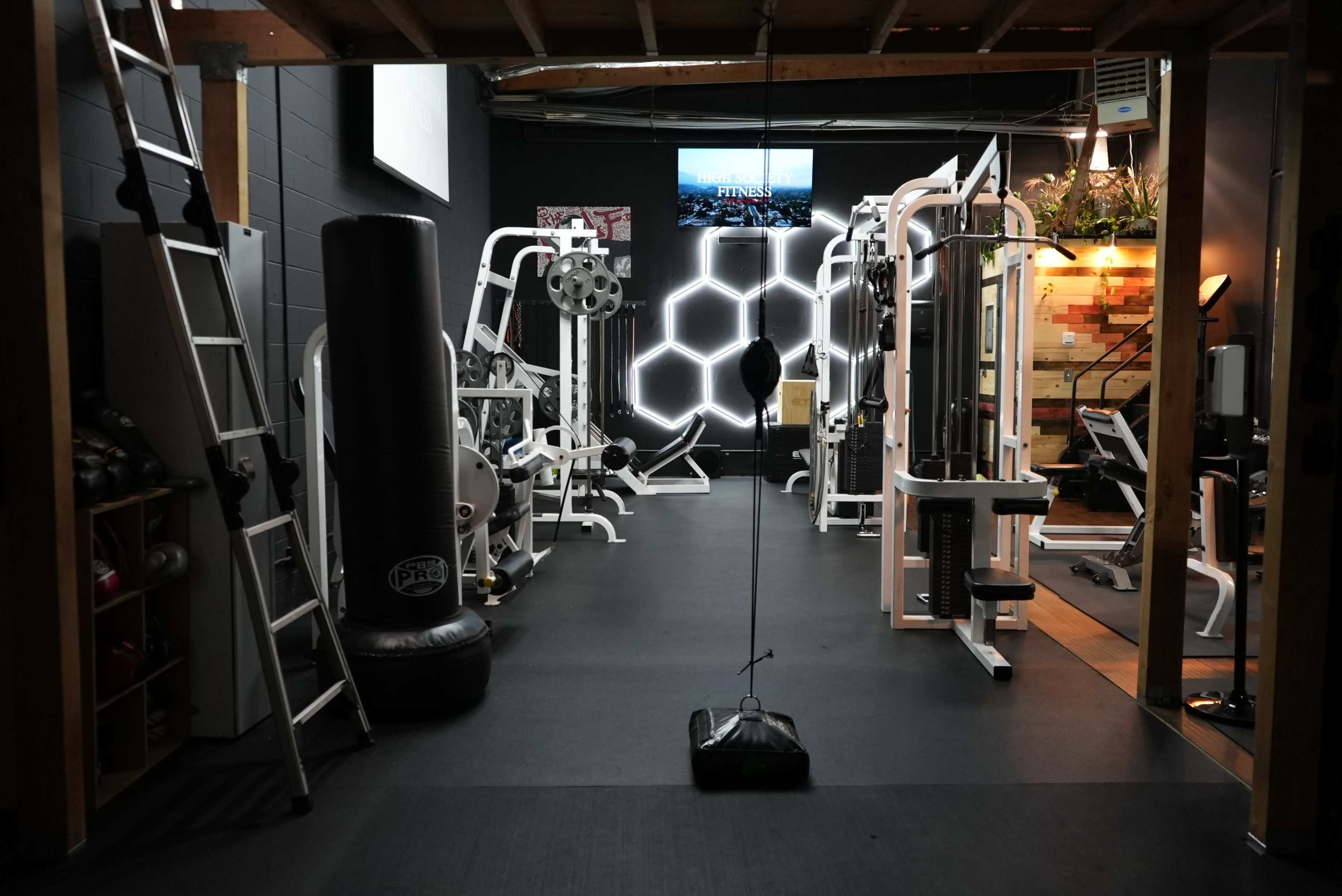 A gym interior equipped with various exercise machines, a boxing bag, and a television mounted on the wall.