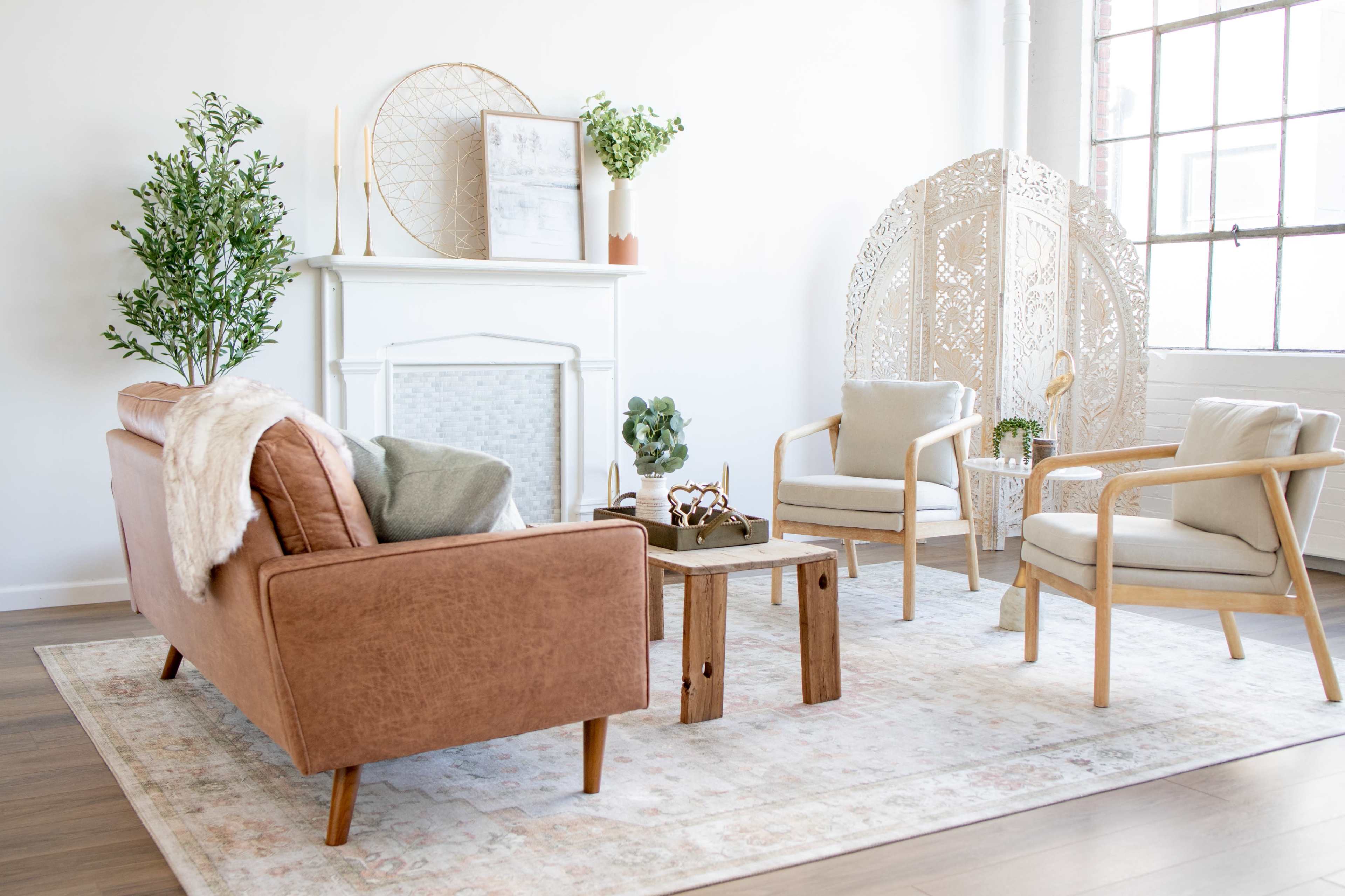A bright, modern living room featuring a brown sofa, light-colored armchairs, a small wooden coffee table, and decorative plants.