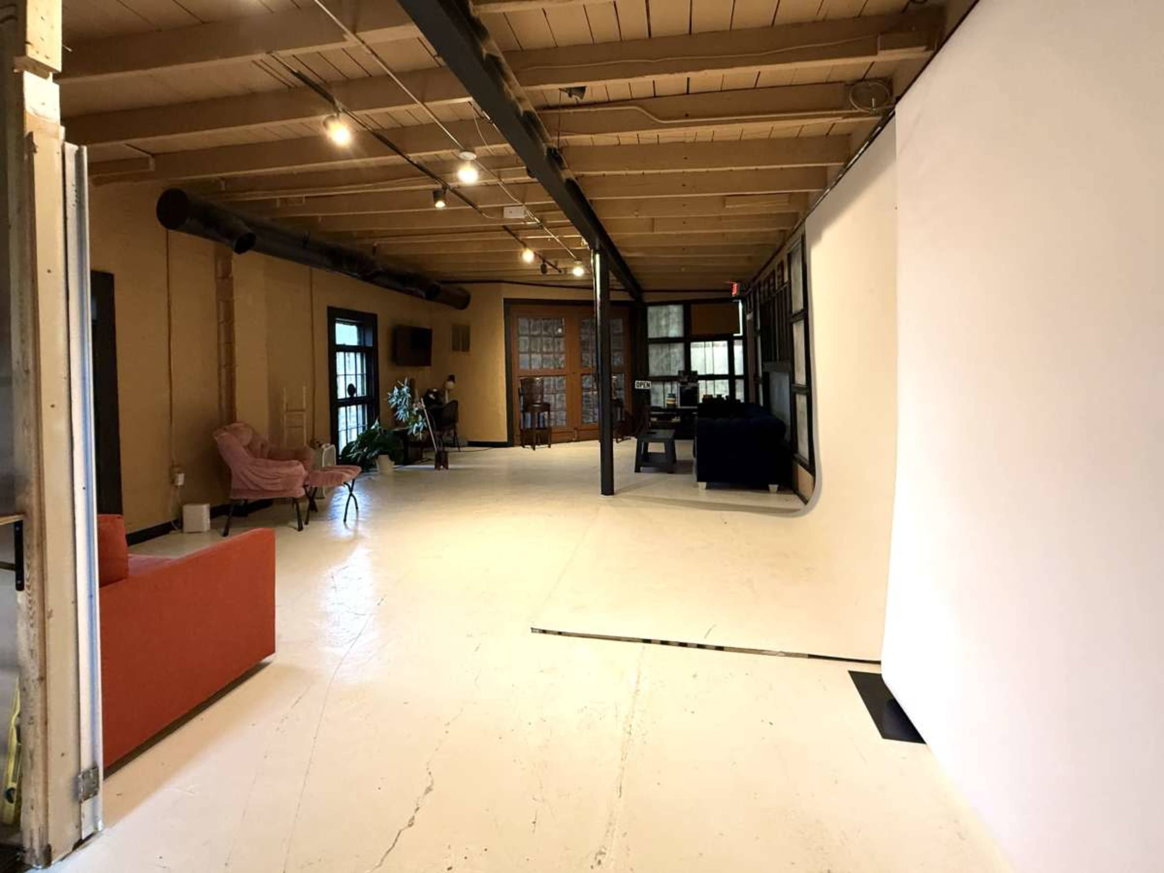 The image shows a spacious interior with a light-colored floor, a pink couch on the left, and a white backdrop in the corner, suggesting a photo studio or creative space.
