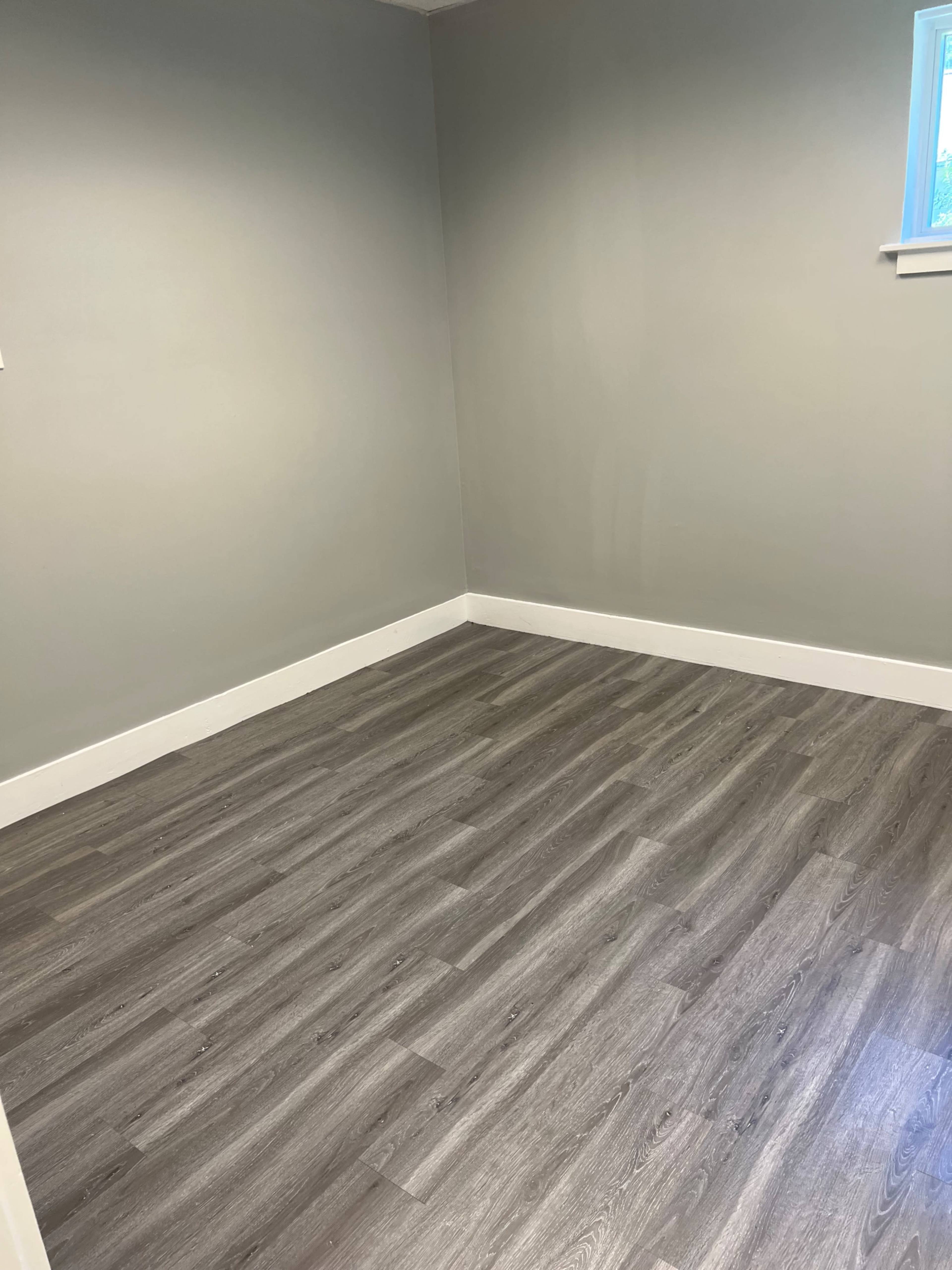 A vacant room with gray walls and new laminate flooring.