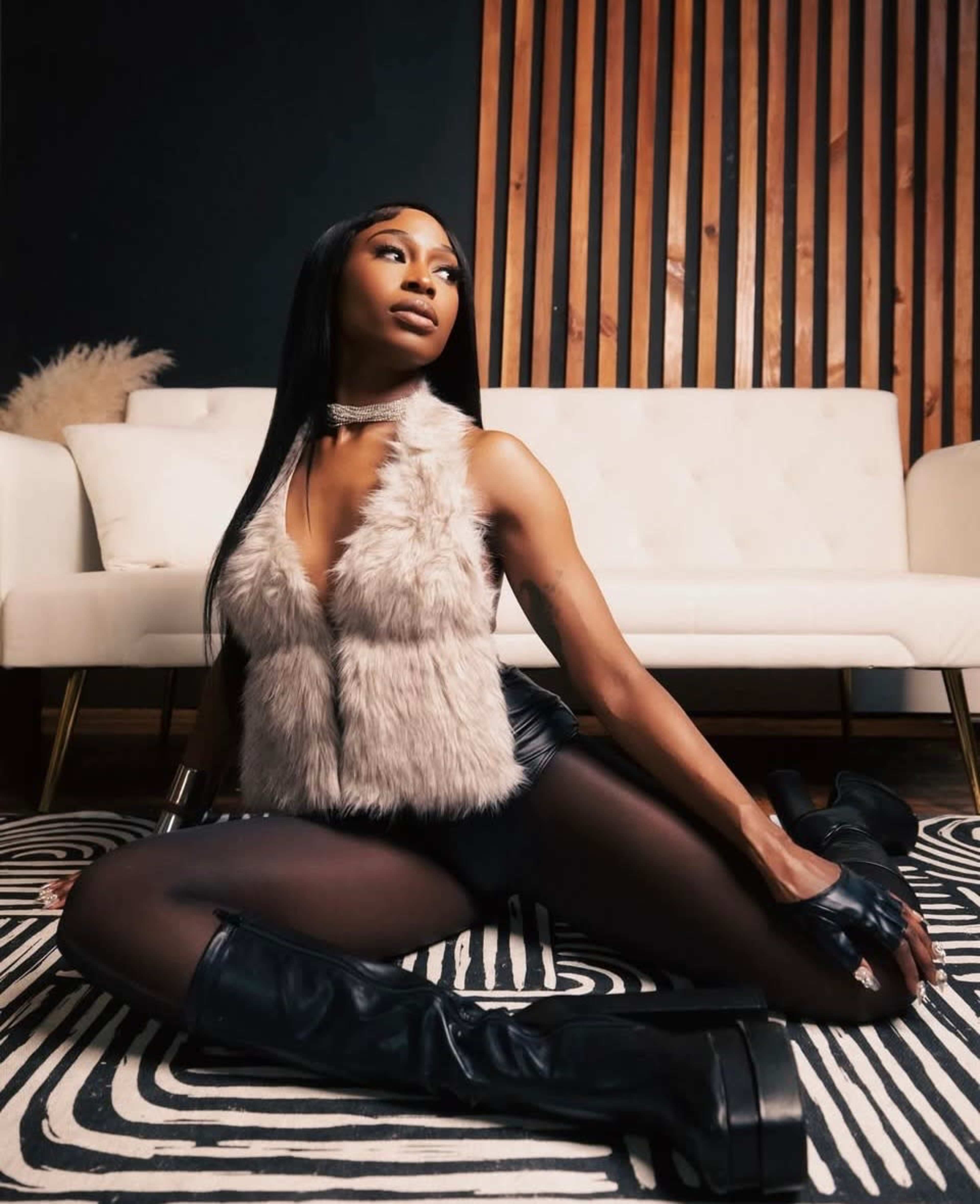 A person wearing a fur vest and thigh-high boots poses on a patterned rug in a modern interior setting.