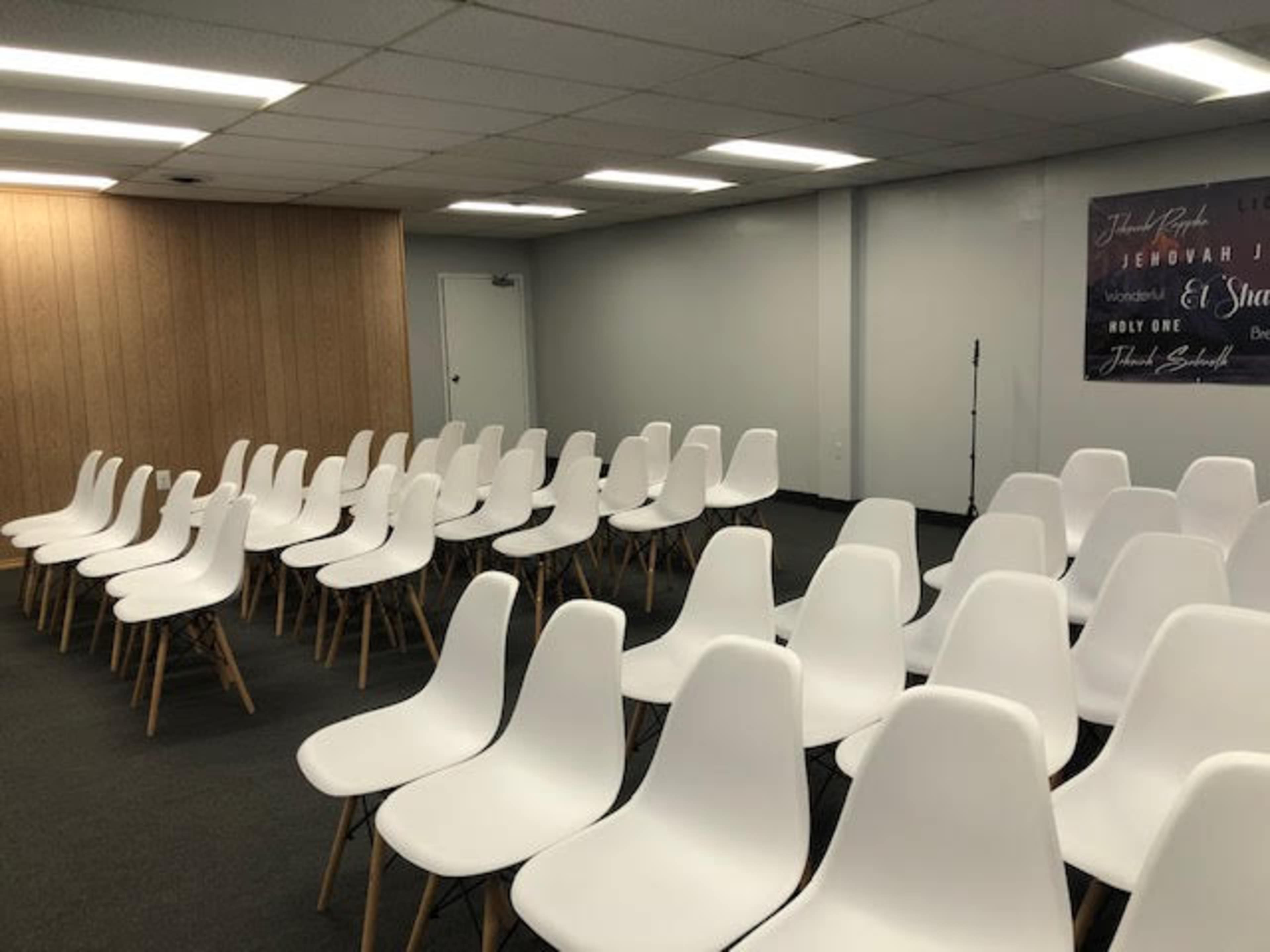 A row of white chairs is arranged in a spacious indoor setting with wood-paneled walls and a promotional banner in the background.