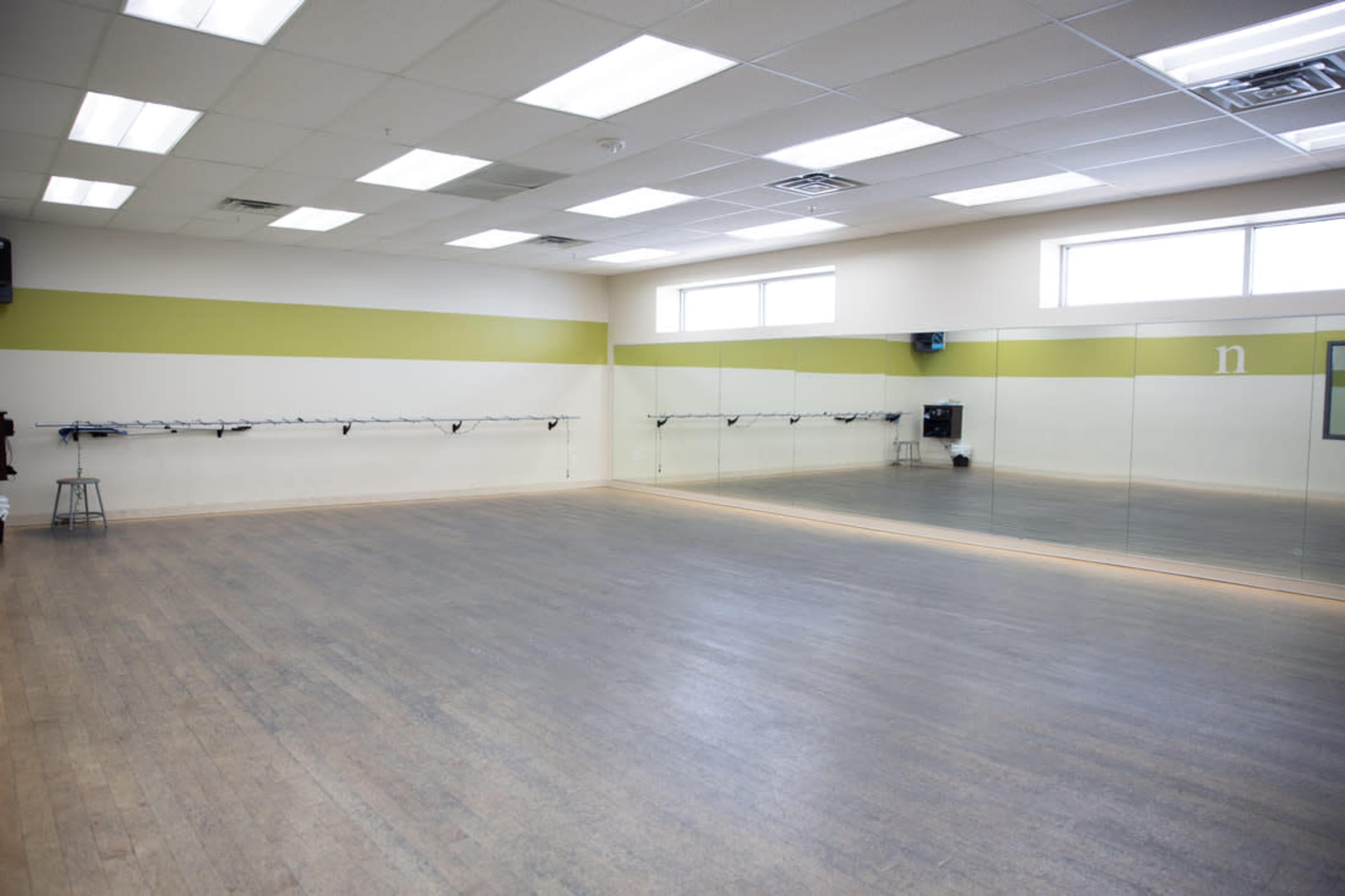 A spacious dance studio with a wooden floor, mirrored walls, and wall-mounted barres.