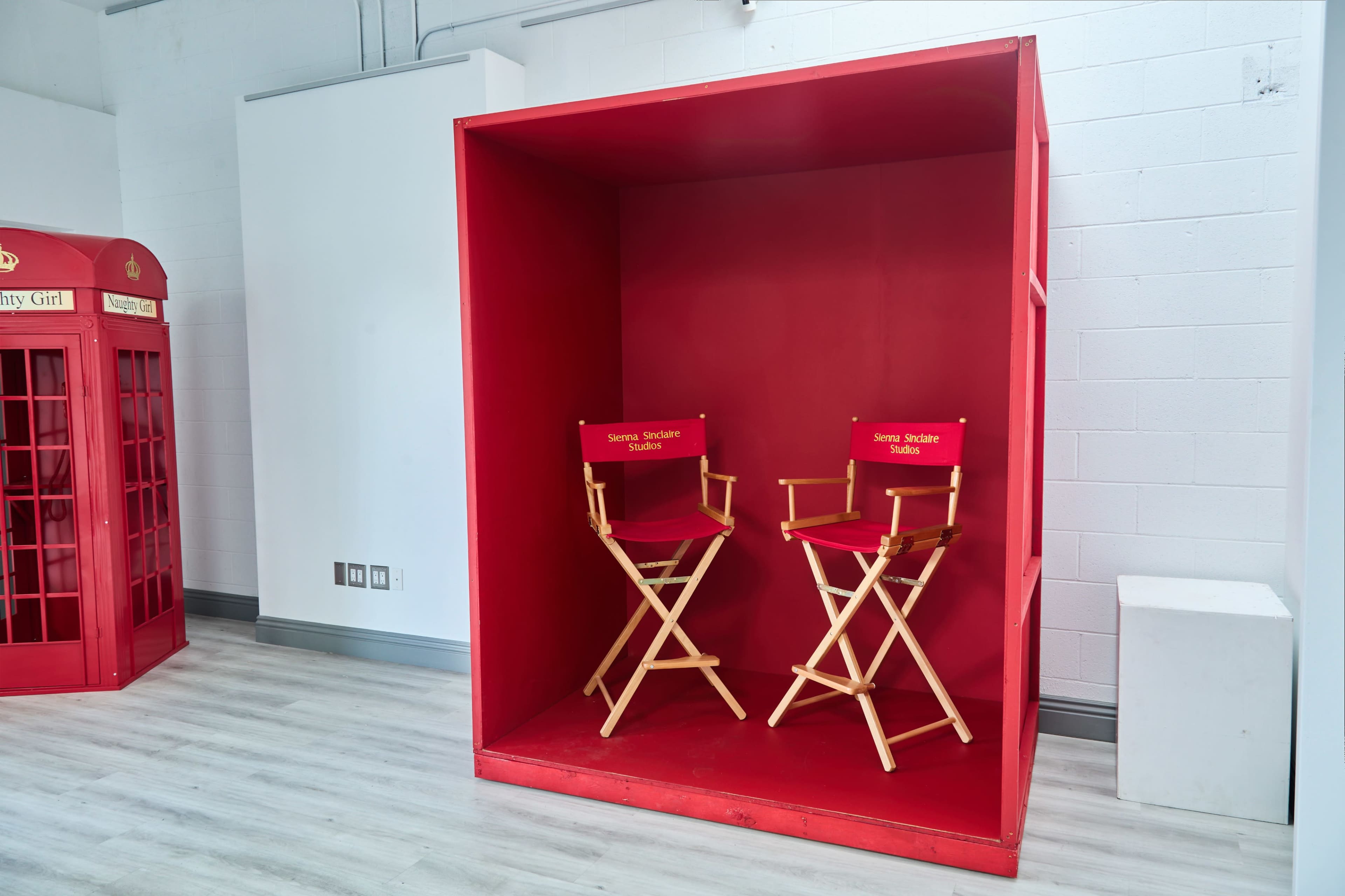 The image features a large red box with two wooden director's chairs inside, labeled "Jerome Stokes" on the backs, set against a white wall.