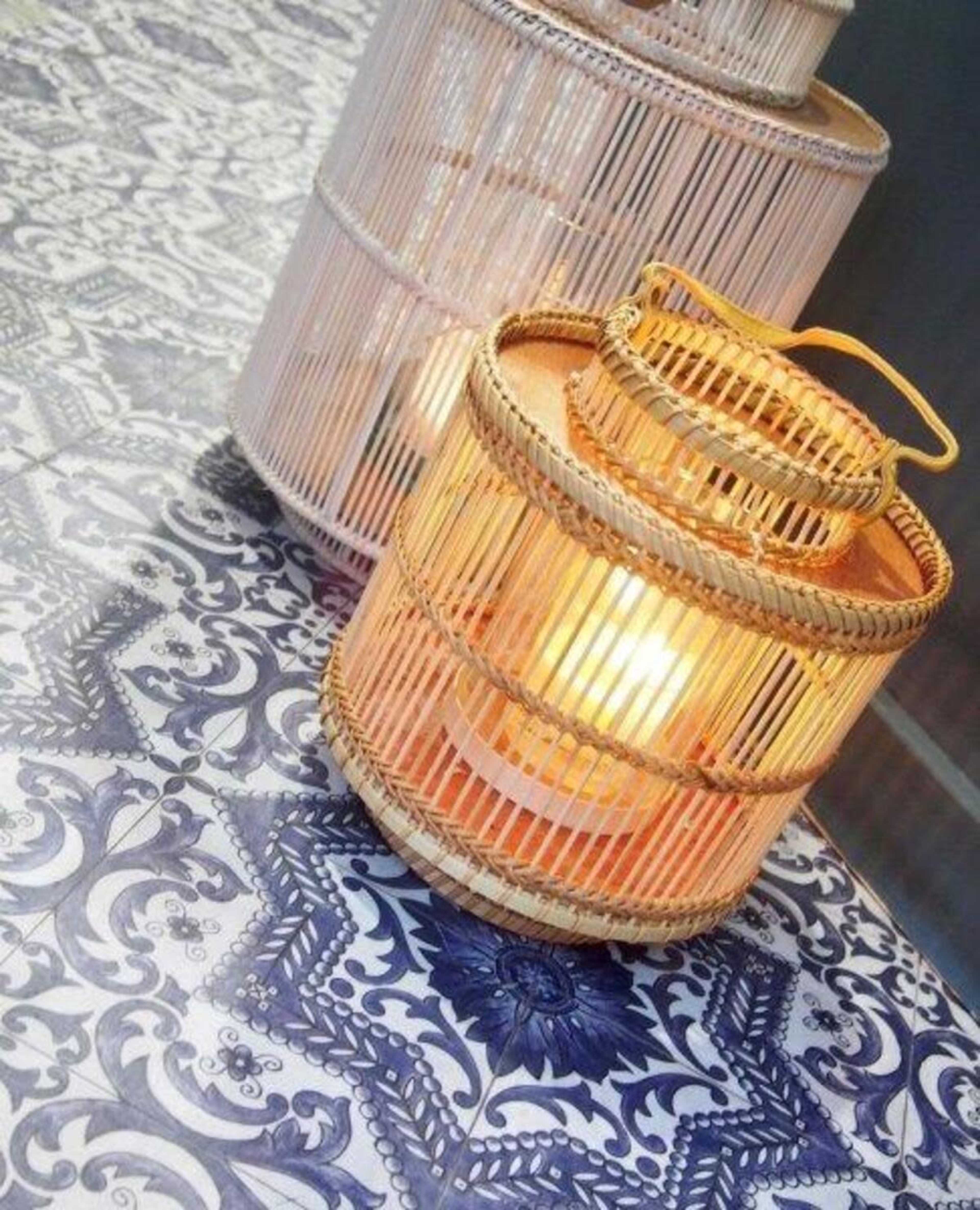 A woven lantern with a warm light sits on a patterned blue tile floor.