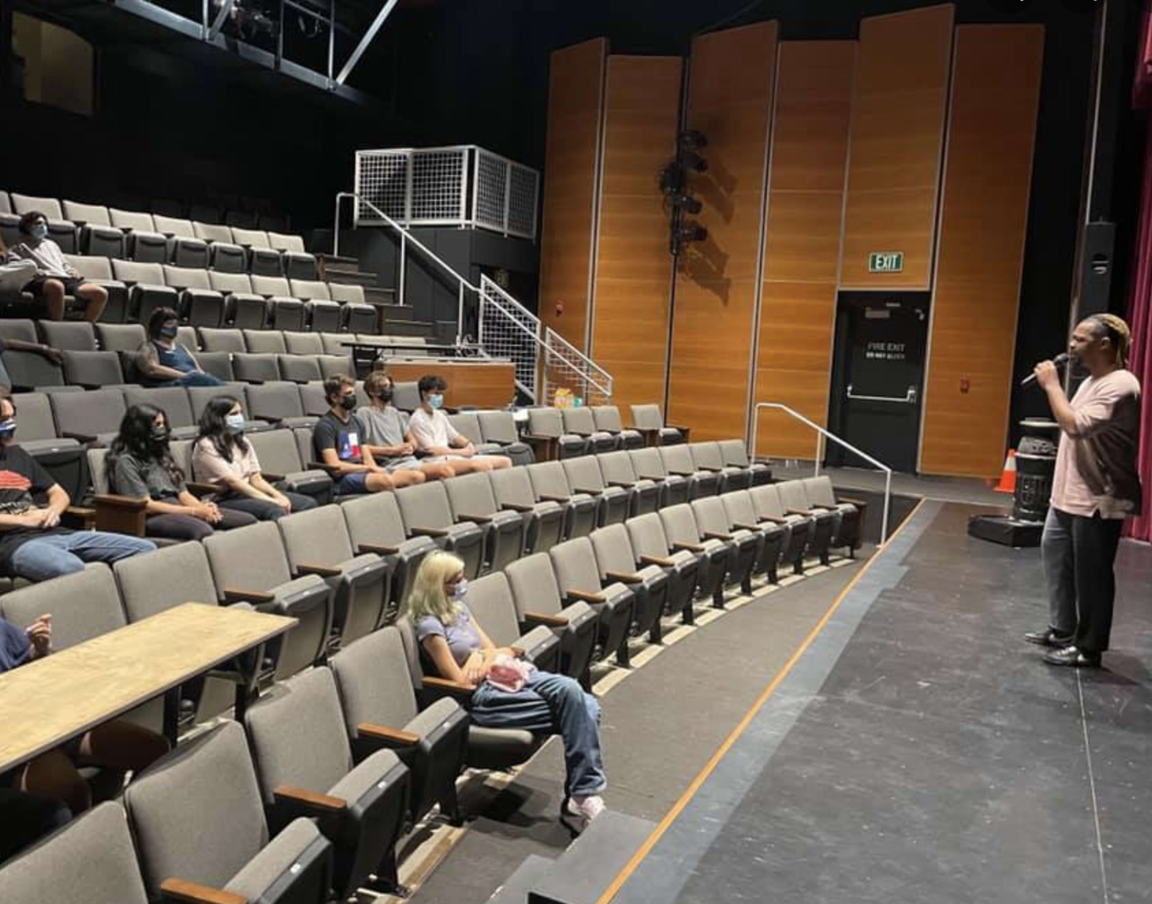 A speaker addresses a small audience seated in a theater.