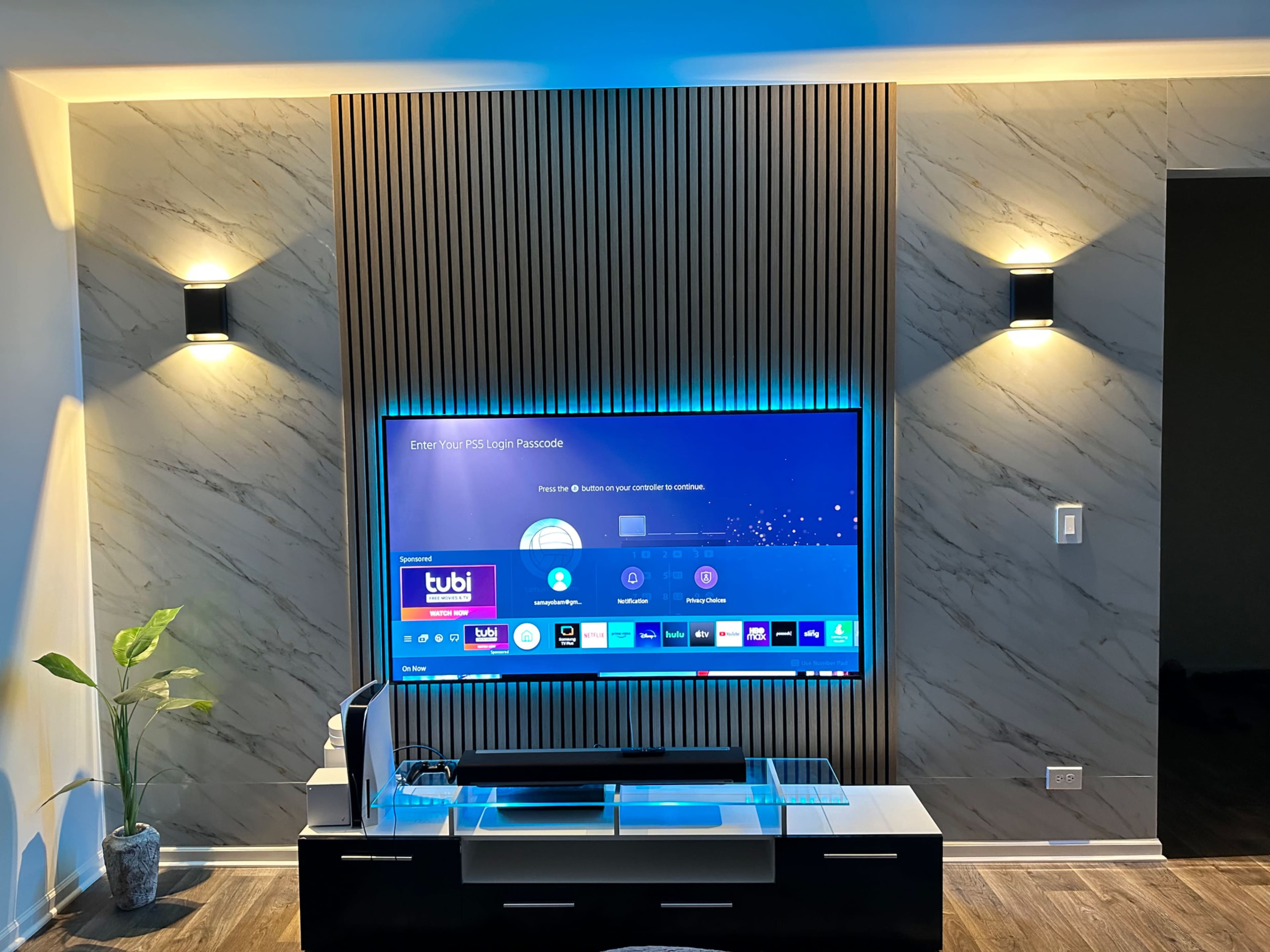 A large flat-screen TV is mounted on a textured wall, with a sleek black media console below and contemporary wall sconces flanking the screen.