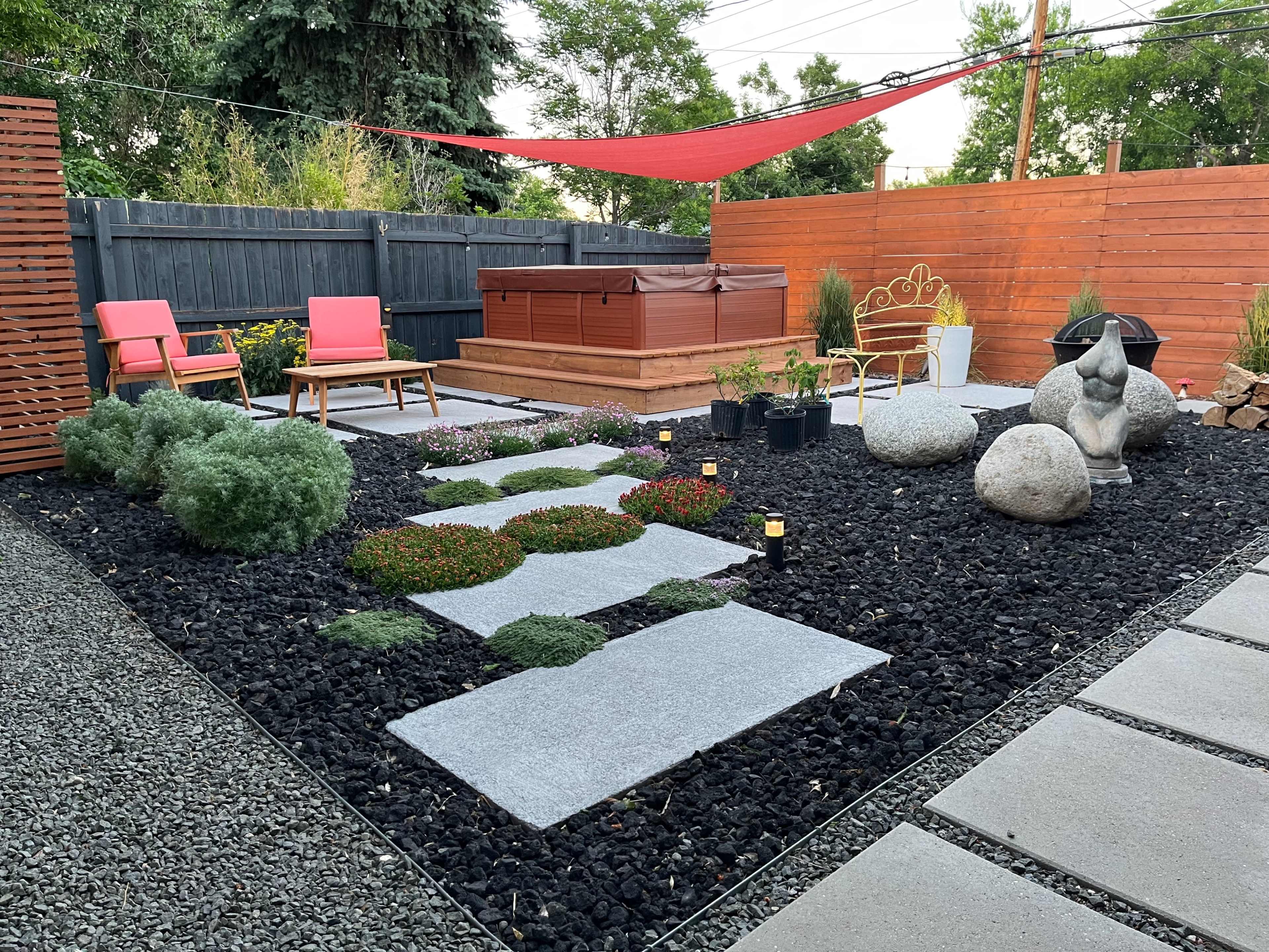 The image depicts a landscaped backyard featuring a hot tub surrounded by stone pathways, decorative rocks, and two pink loungers under a red canopy.