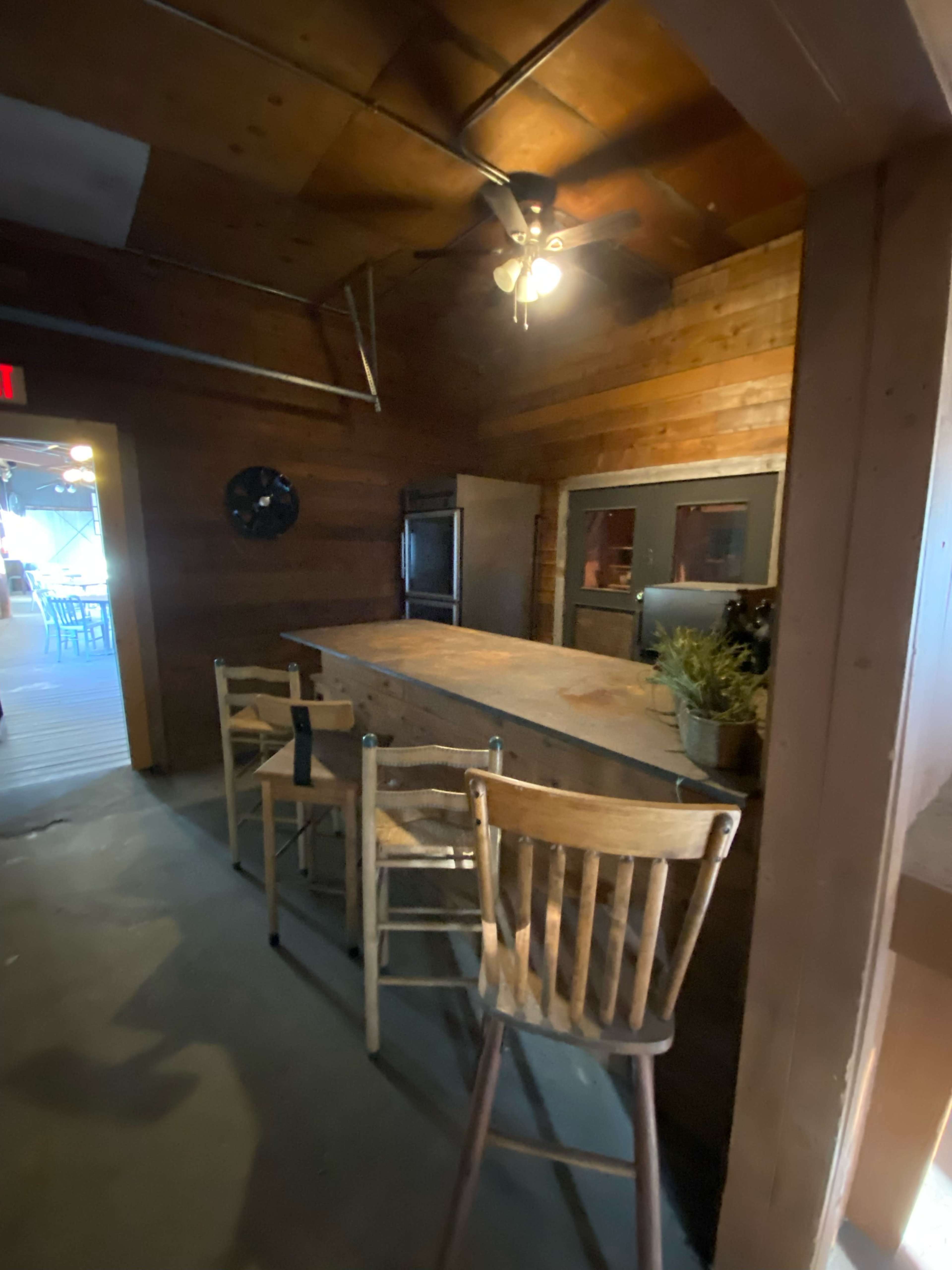A rustic wooden bar area with several empty wooden stools and a ceiling fan.