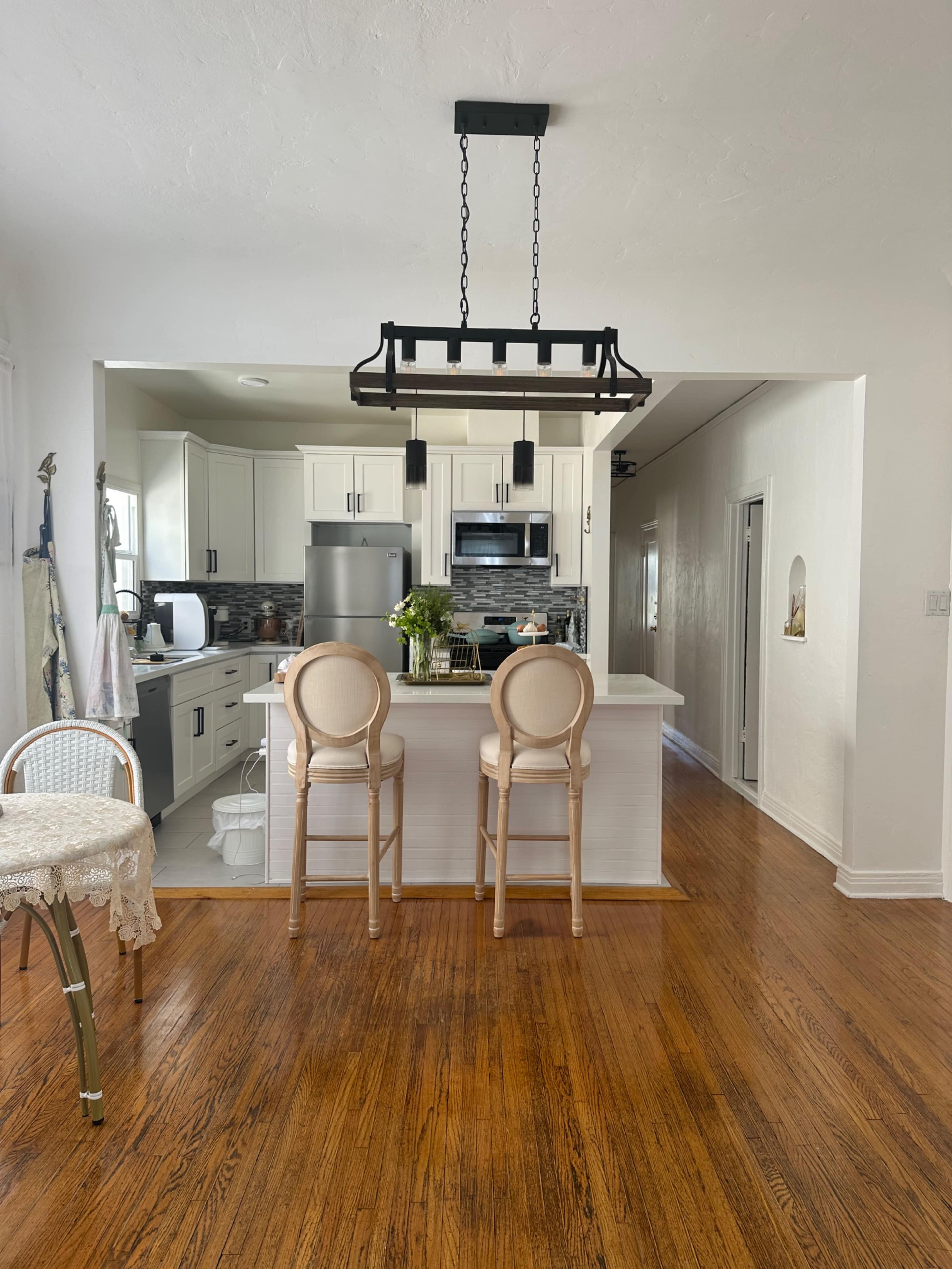 The image shows a modern kitchen with white cabinetry, a stainless steel refrigerator, and two bar stools at a counter.